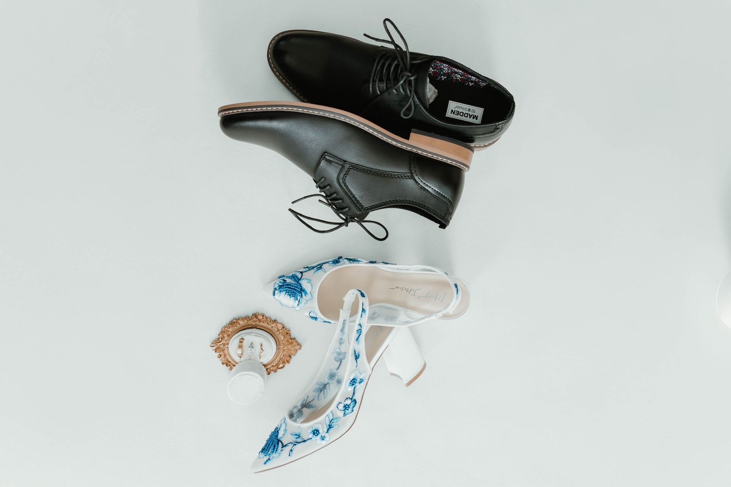Overhead view of black leather dress shoes and blue floral ballet flats arranged on white background.