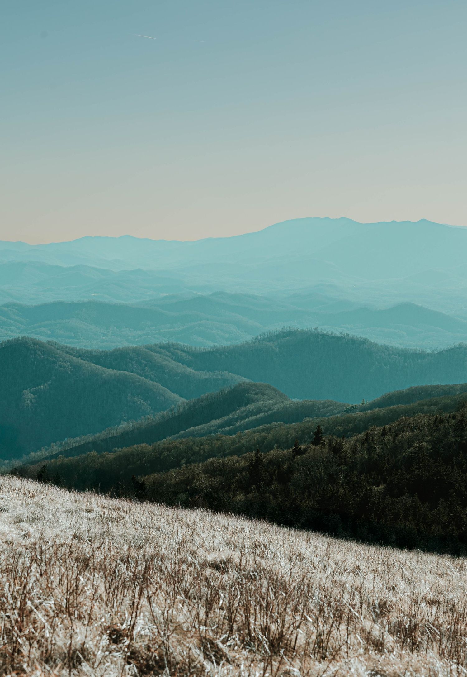 Snow-covered mountain ridges stretch into the distance under a pale blue sky in a panoramic winter landscape.