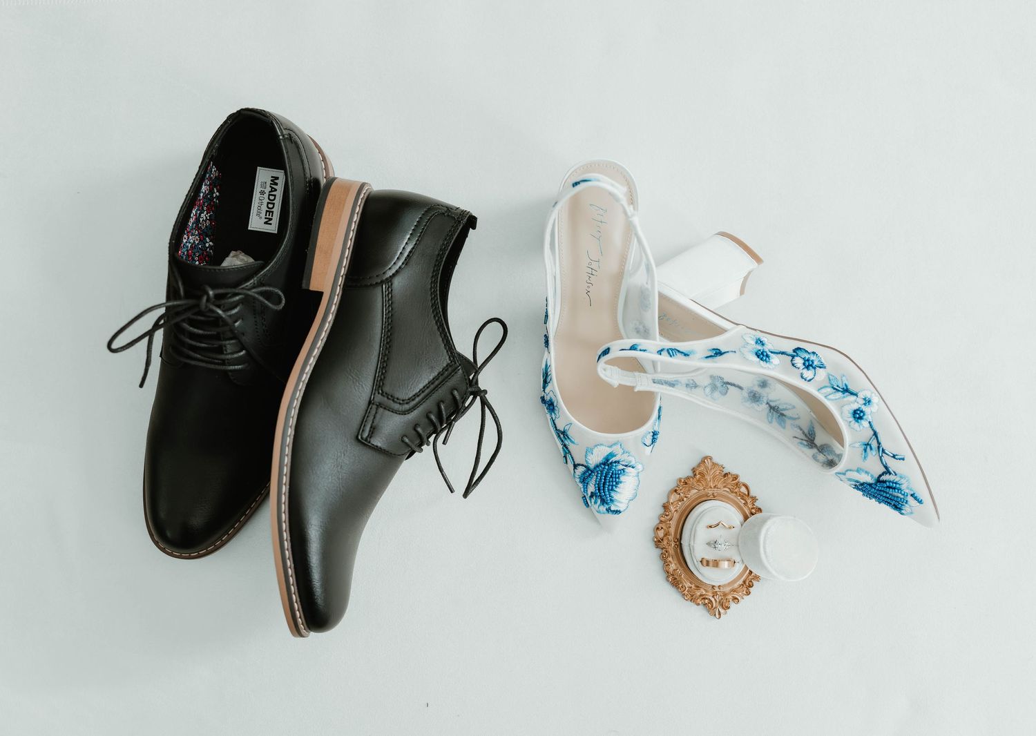 Wedding shoes arranged on white background with black leather dress shoes and delicate white bridal heels with blue details.
