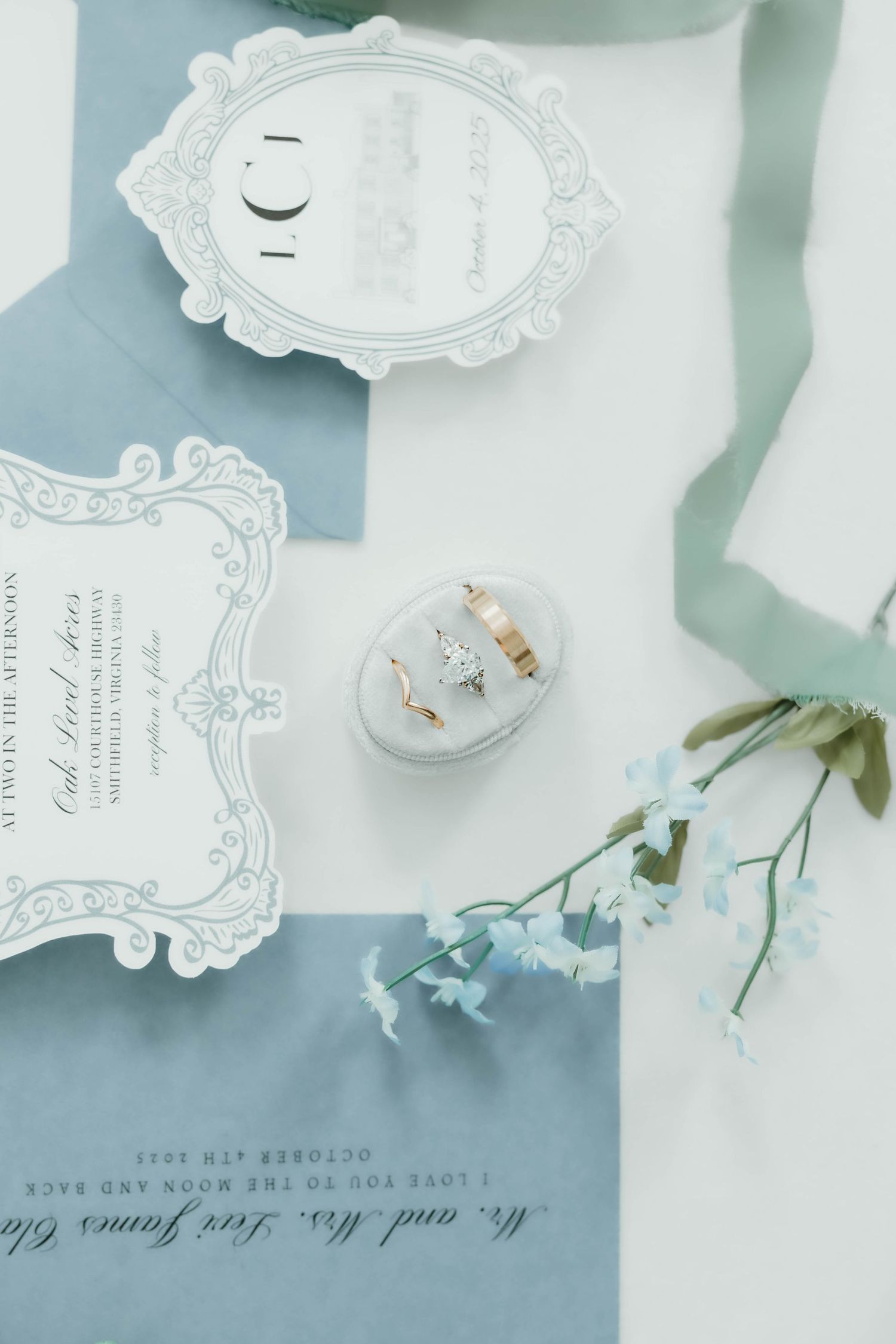 Elegant wedding stationery layout with ornate white frames and delicate floral elements on a soft blue background.