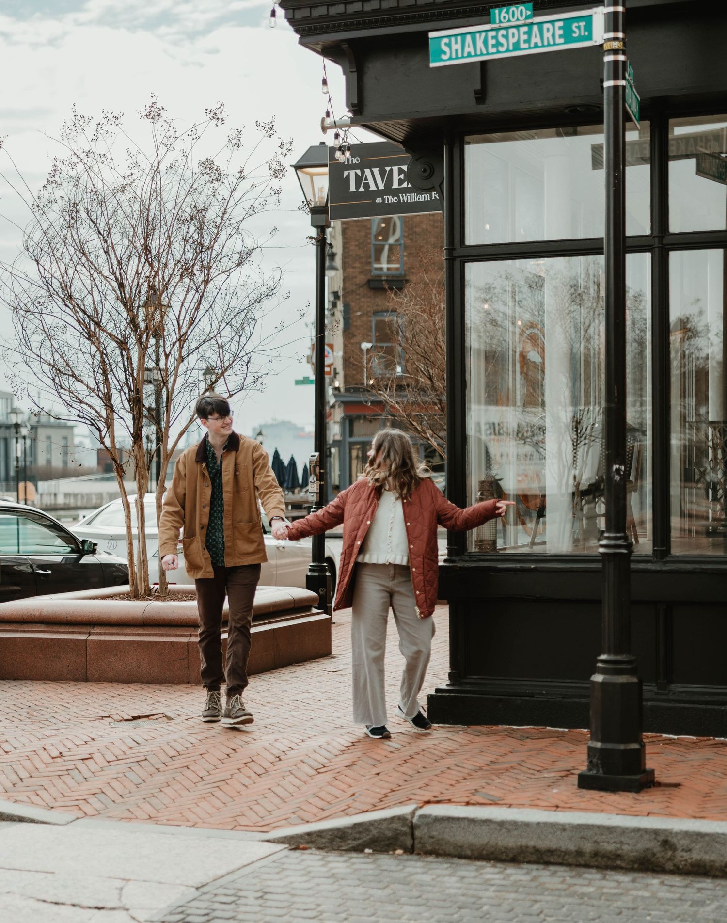 A couple walks down a historic brick street in winter with Shakespeare Road sign visible in the background.