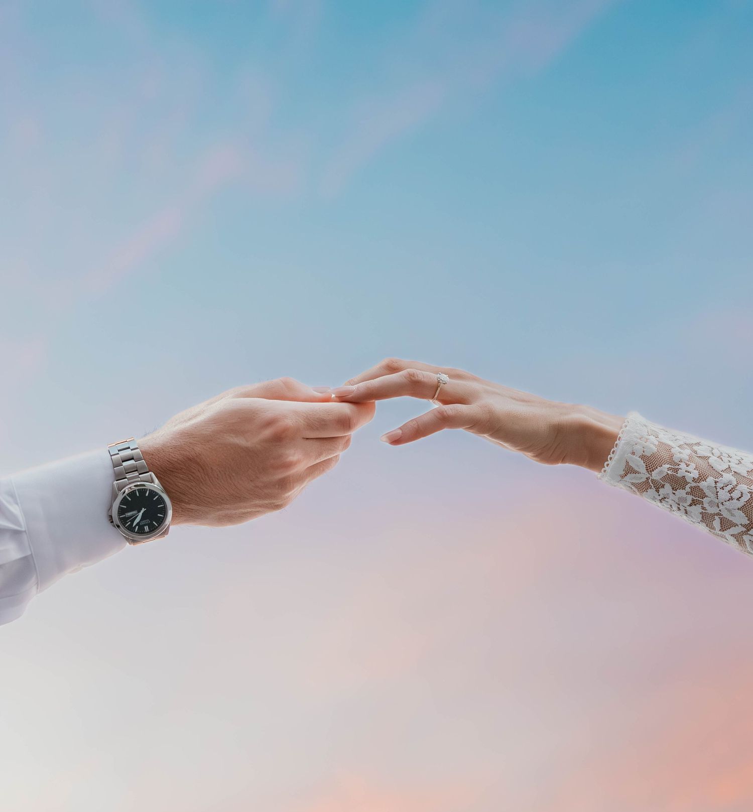 Two hands reaching towards each other against a soft pastel sky backdrop, with one wearing a silver watch.