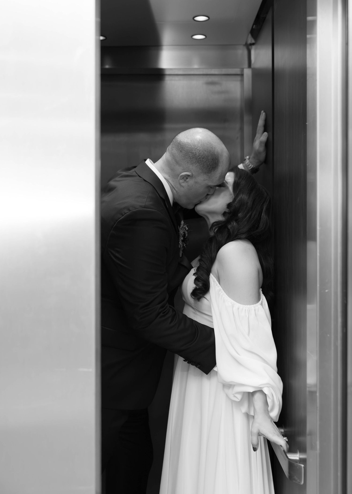 Black and white photo of people in white dresses and dark suits standing in an elevator.