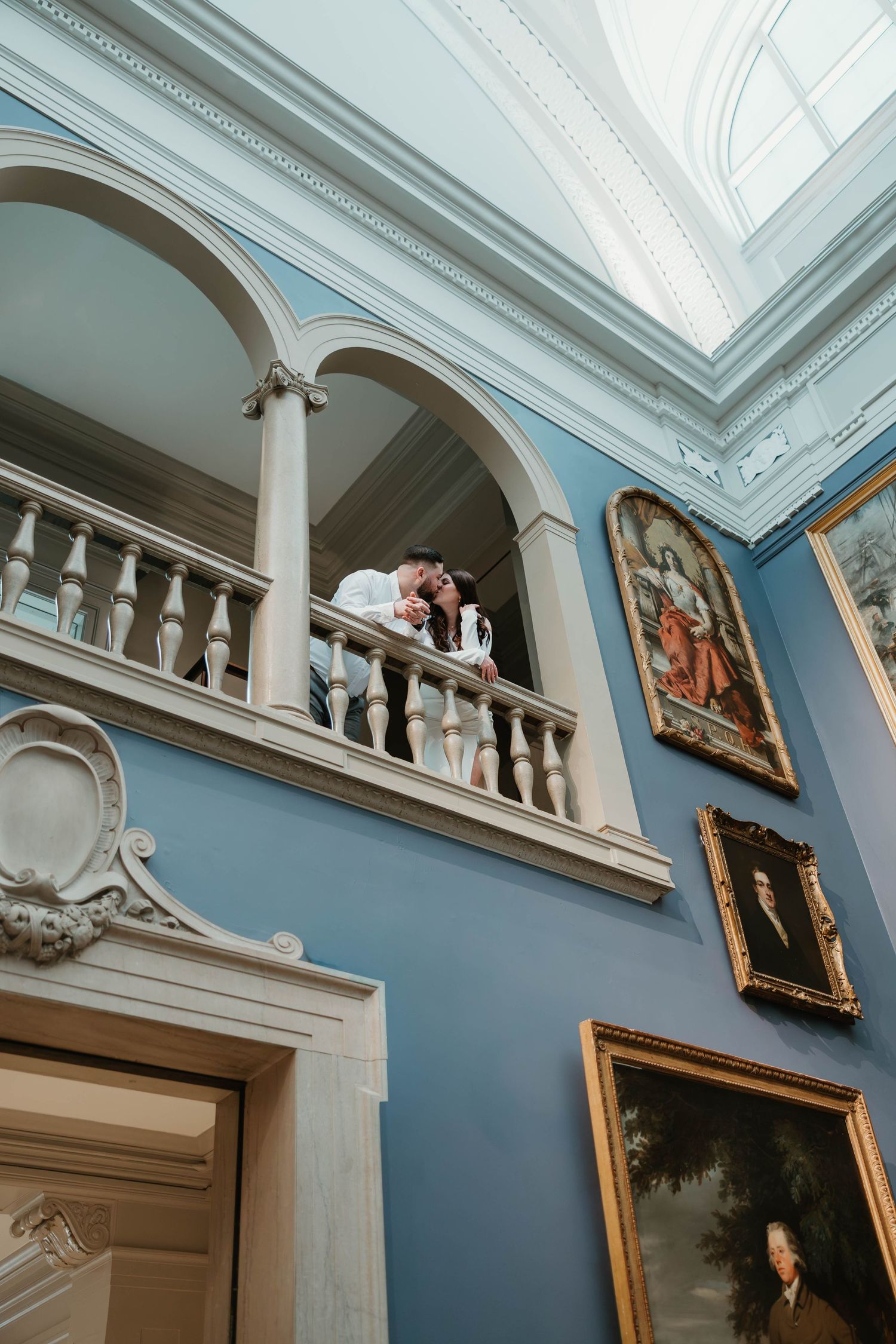 Interior architectural details showing ornate crown molding, blue walls, and classical white columns in an elegant gallery space.