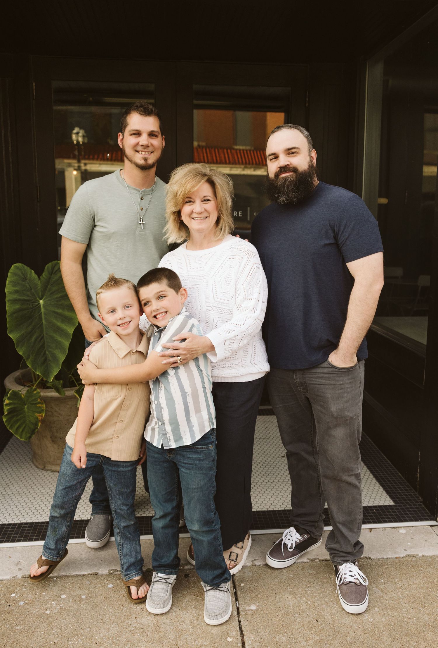 Family of five poses together outside storefront with large tropical plant.