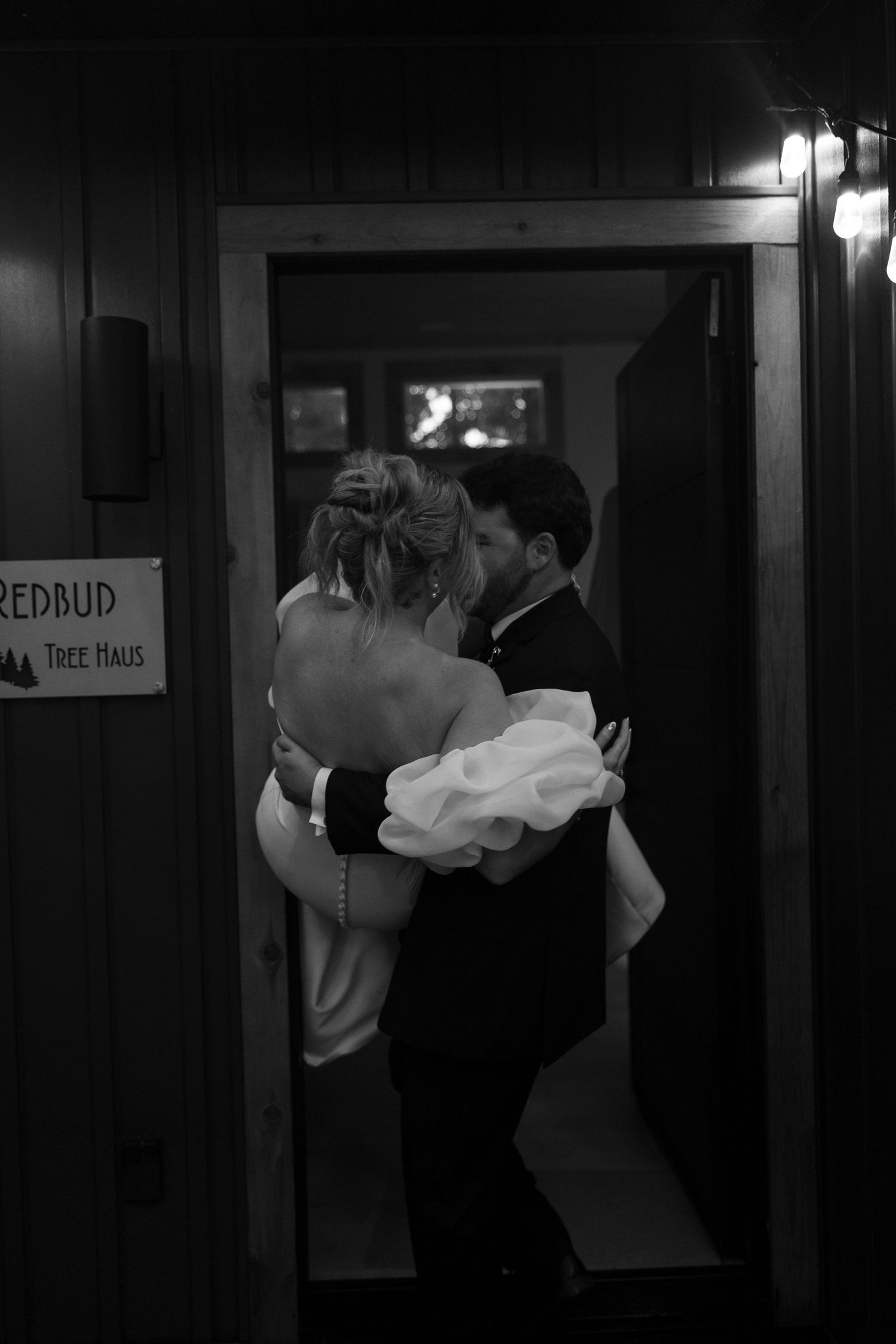 Black and white photo of a couple embracing in a doorway at night.