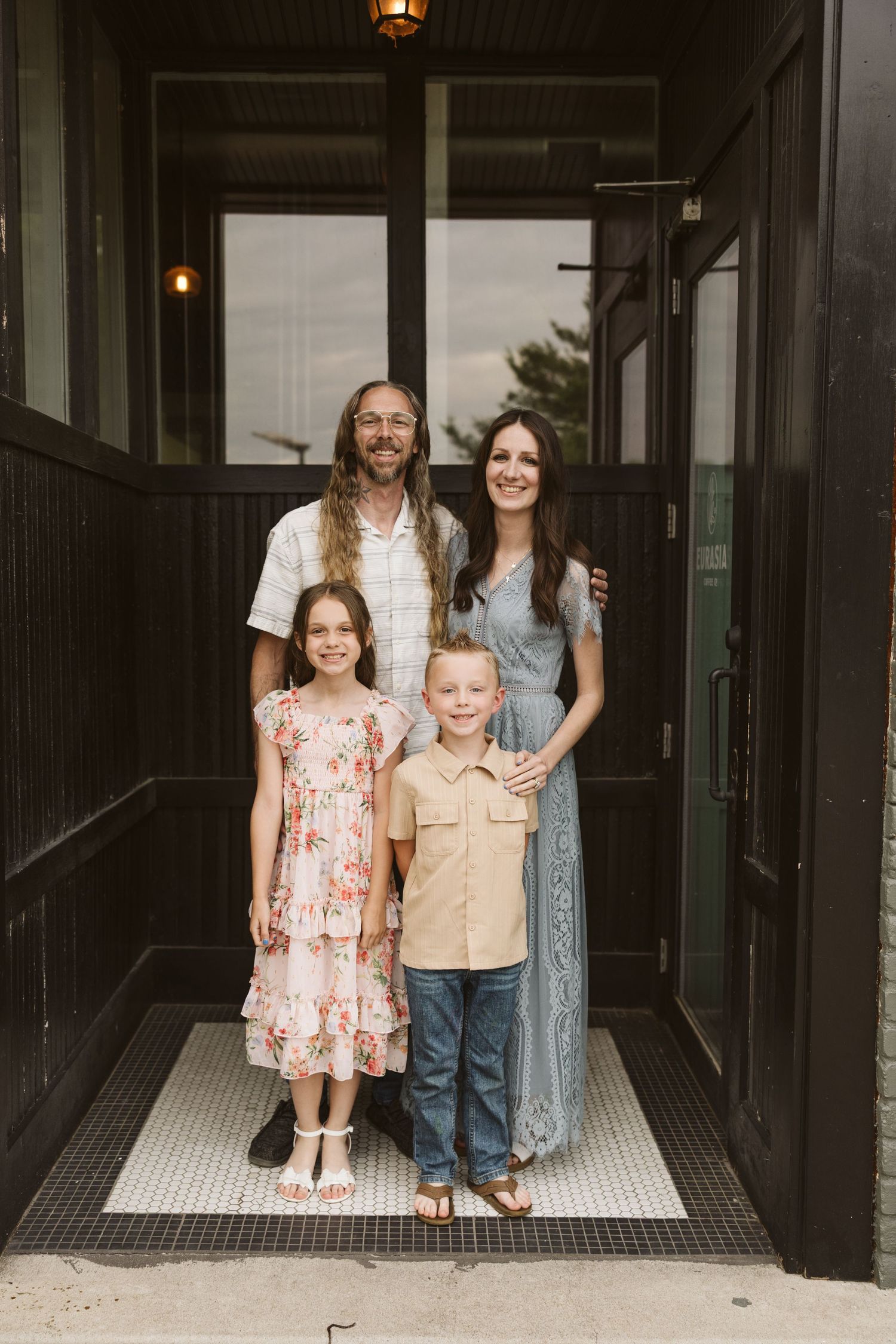 Family of four poses together in dark hallway with ambient lighting.