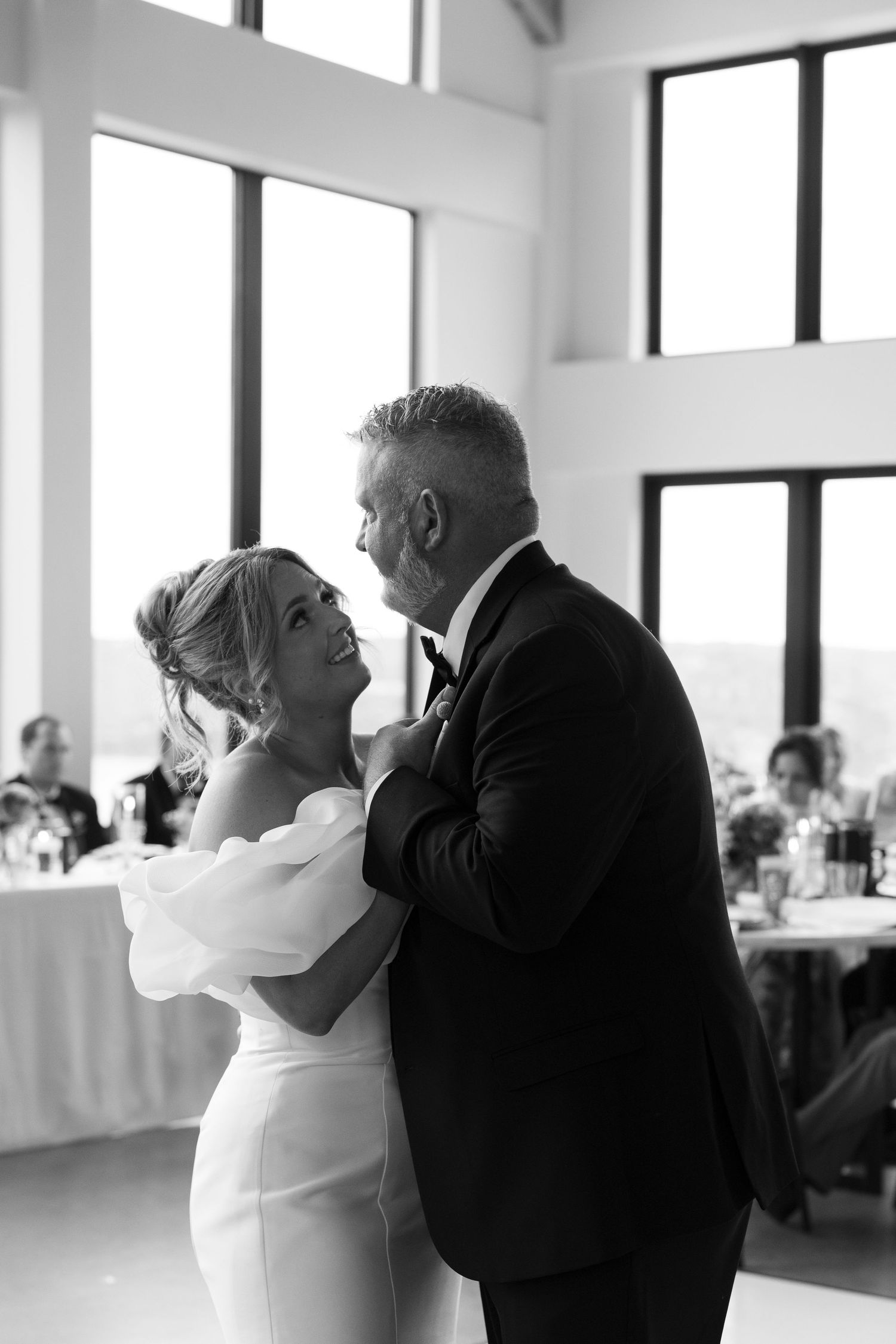 Black and white candid dance sequence in a bright modern reception venue with large windows.