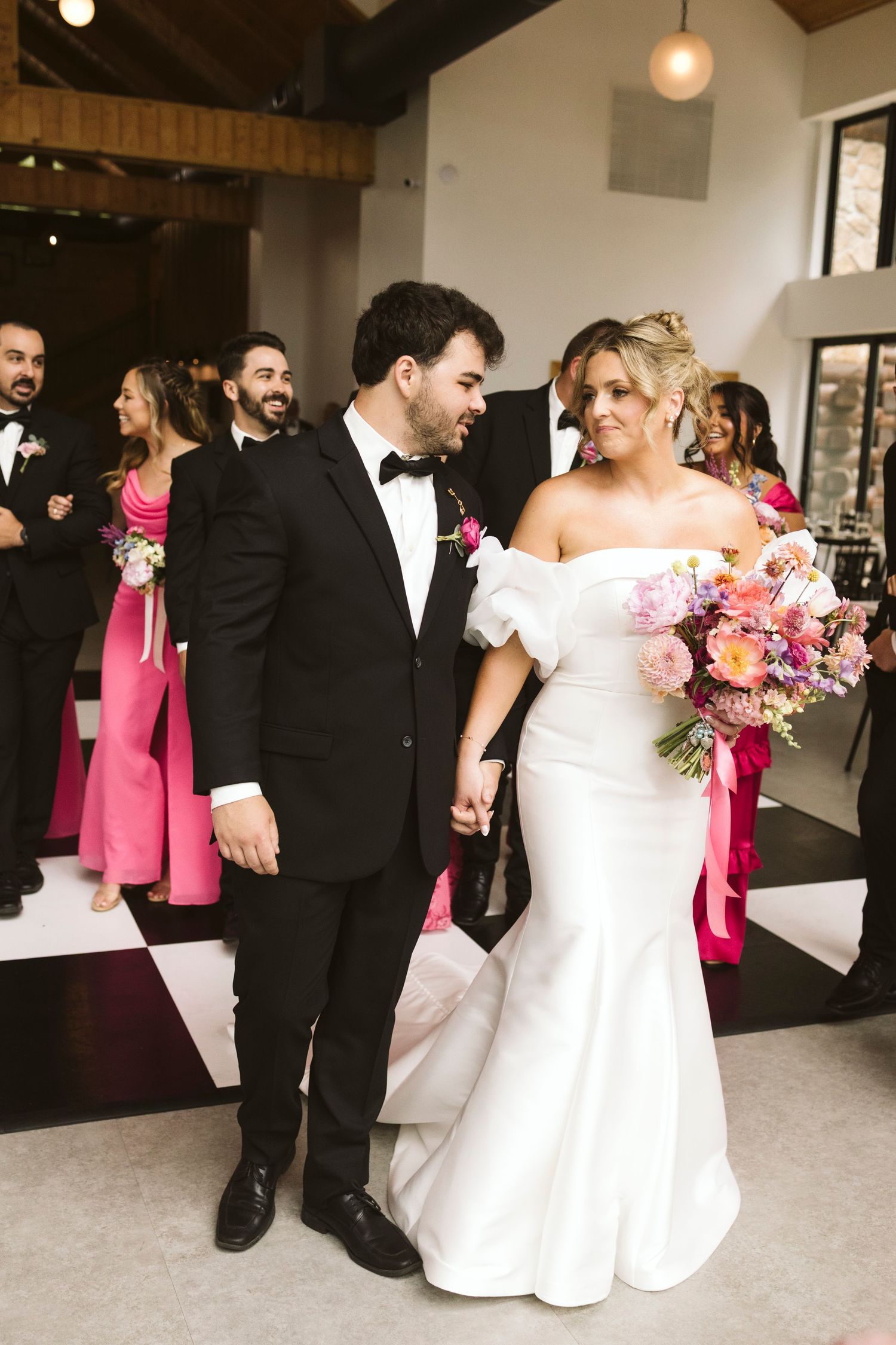Wedding party dancing and celebrating in modern venue with exposed wooden beams.