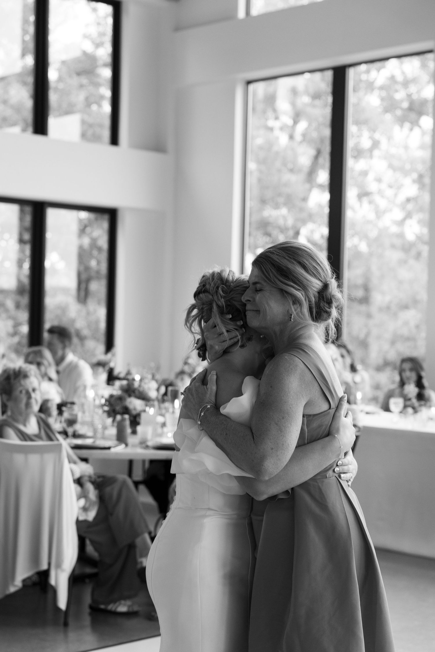 An emotional embrace shared during a wedding reception in a bright, window-filled venue.