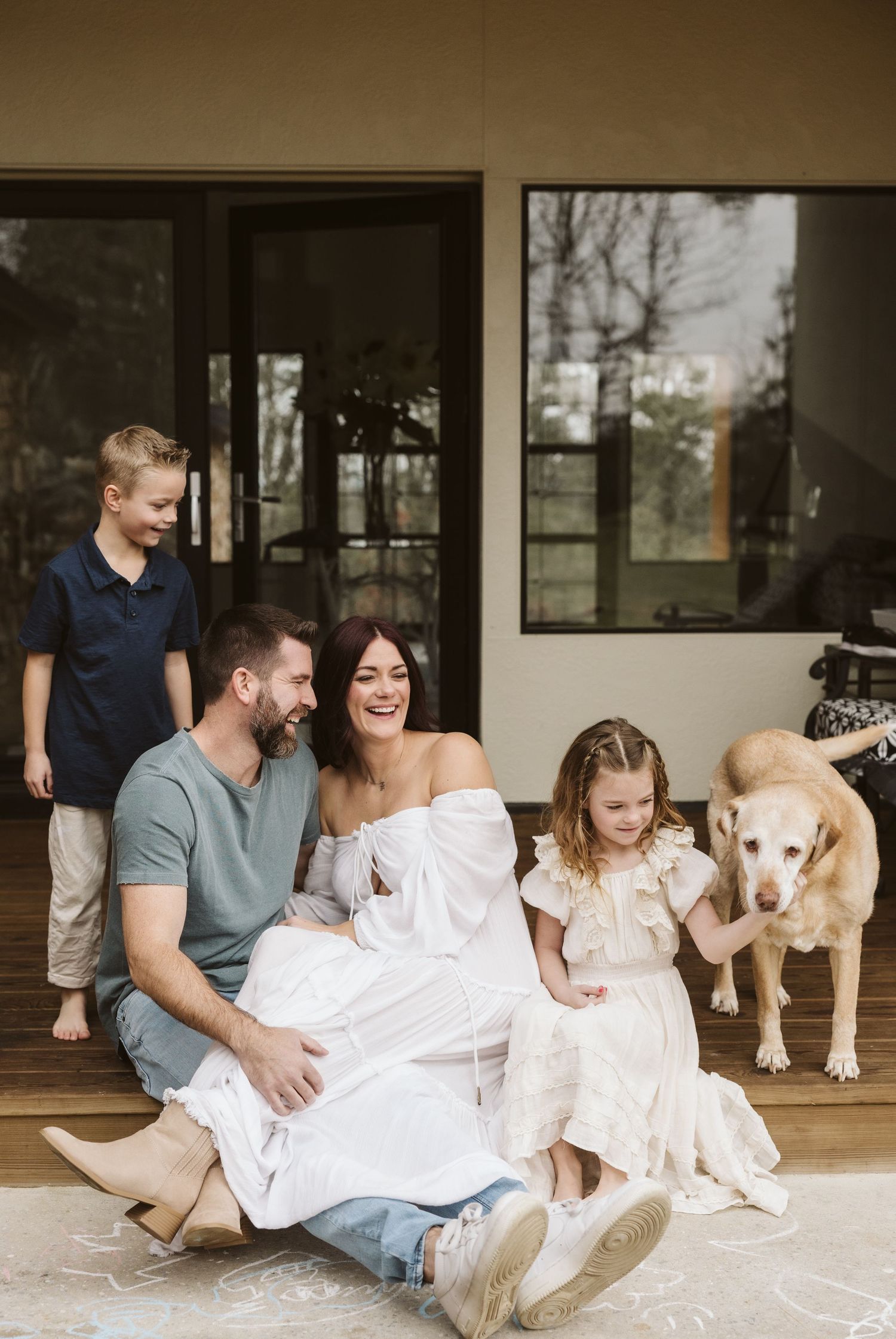 Family and dog relaxing on porch in white outfits during outdoor photoshoot.