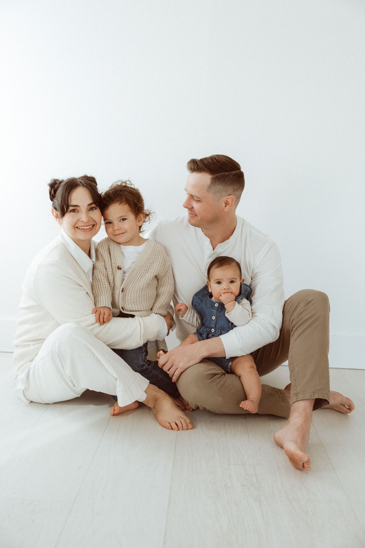 Family with two young children posing for portrait in white studio setting.