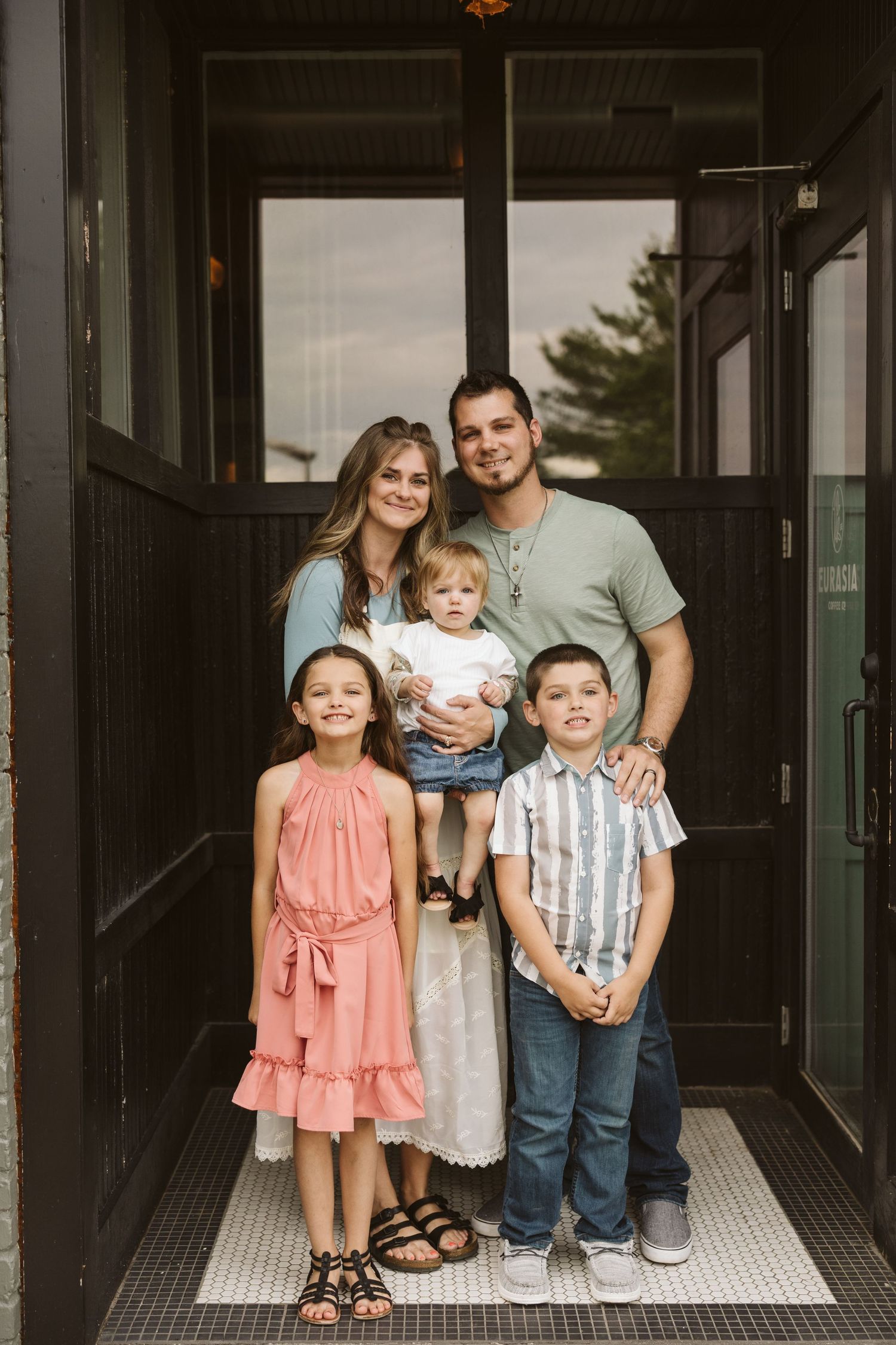 Family of five posing together in a doorway entrance with natural lighting.