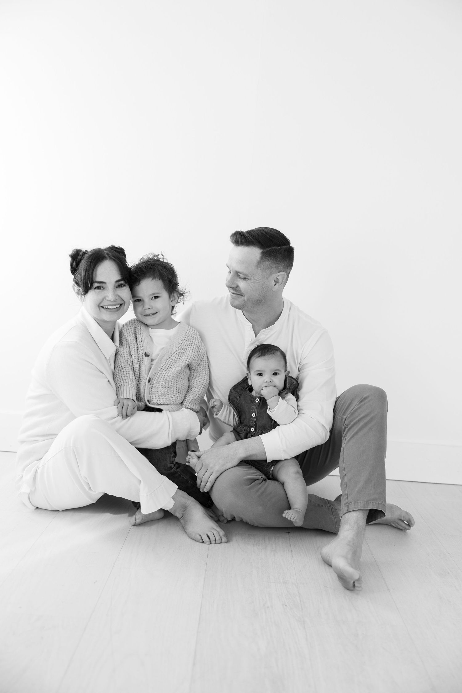 Family of four sitting together in minimalist white studio setting for portrait session.
