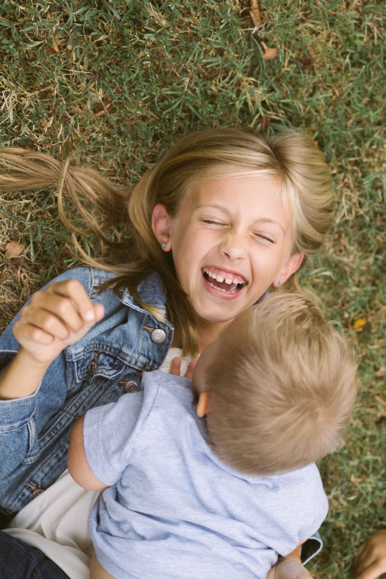 Two children laying on grass laughing and playing together in casual clothes.