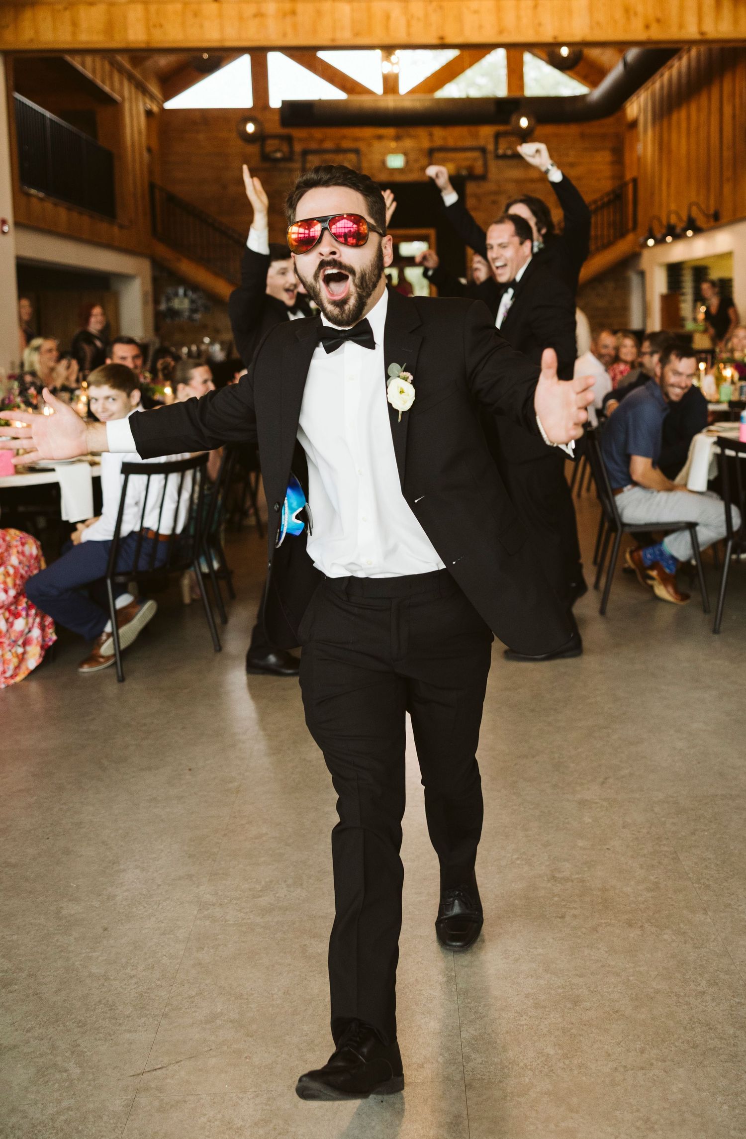 Celebratory moment at wedding reception with guest wearing sunglasses and bowtie.