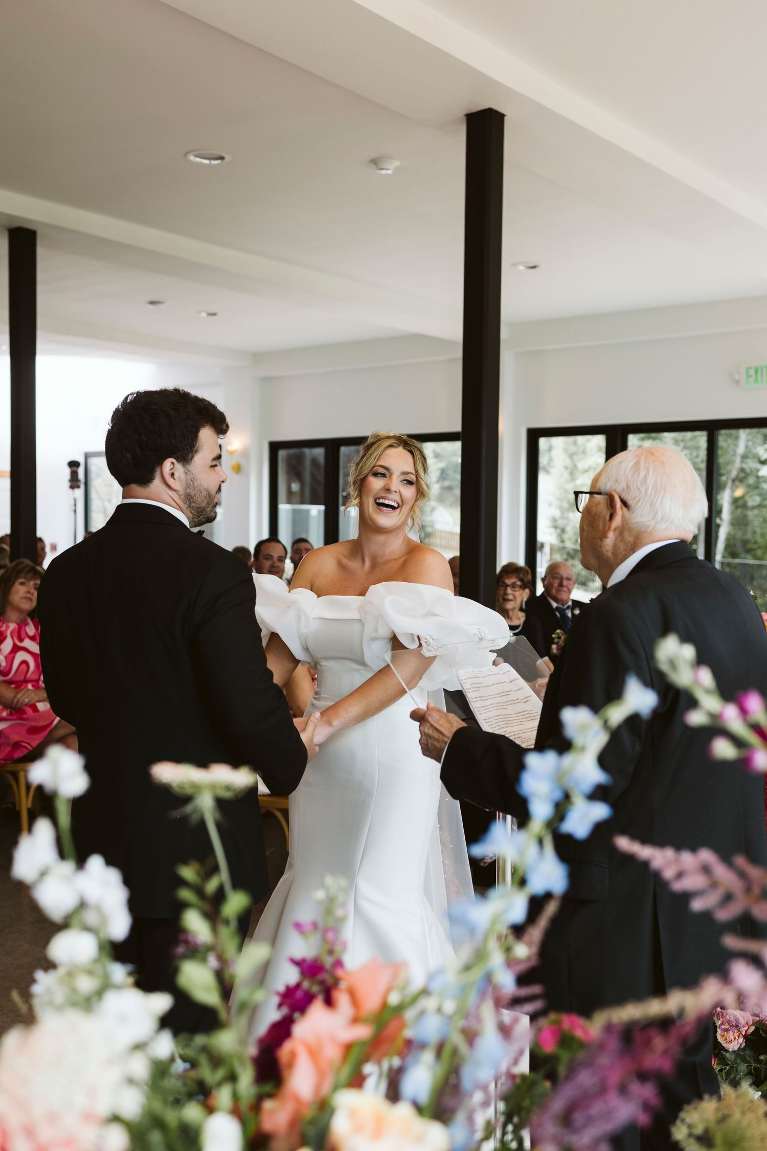 Guests dancing and celebrating at an elegant wedding reception with colorful floral arrangements in the foreground.