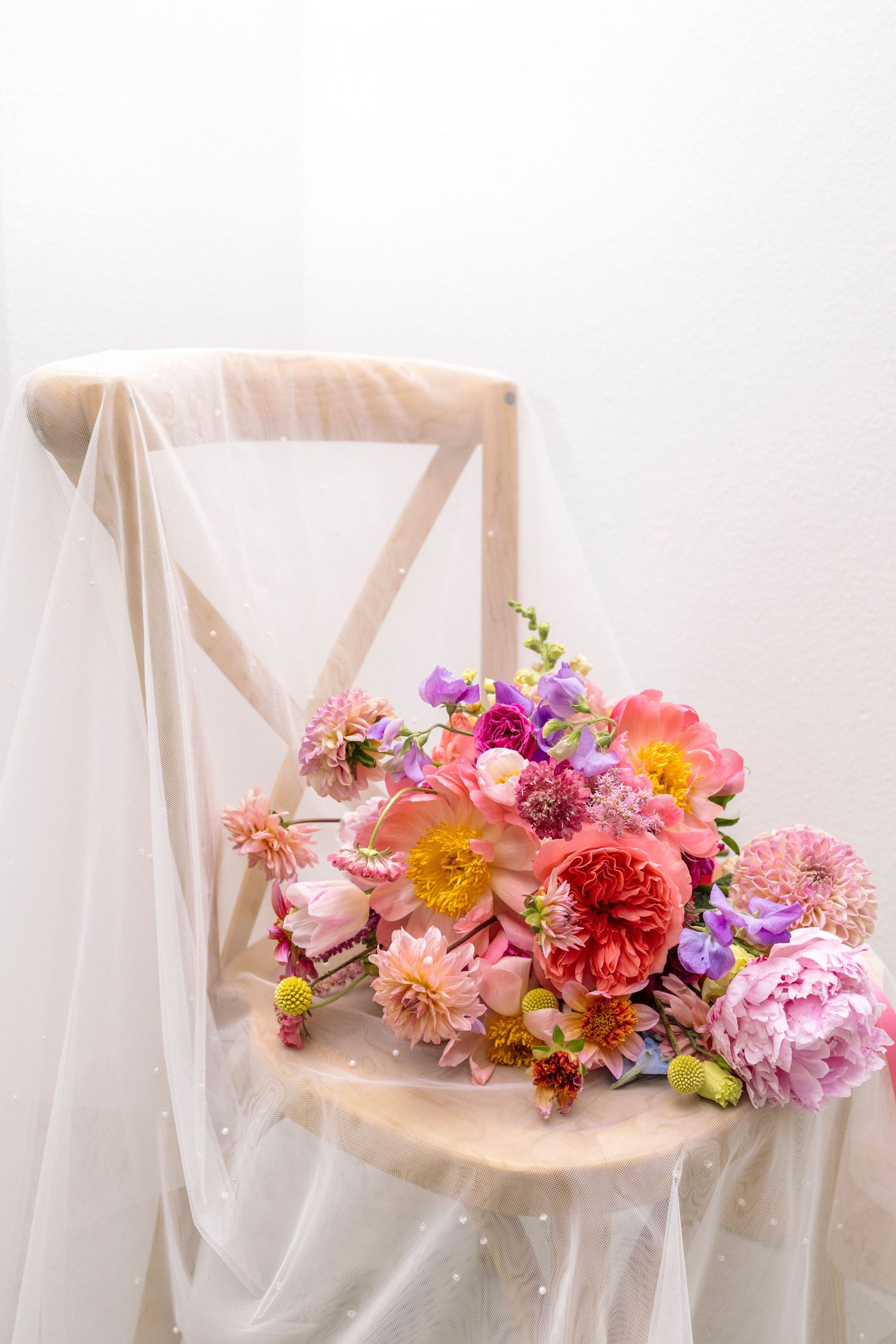 Delicate floral arrangement of pink, purple, and coral blooms adorning white fabric.