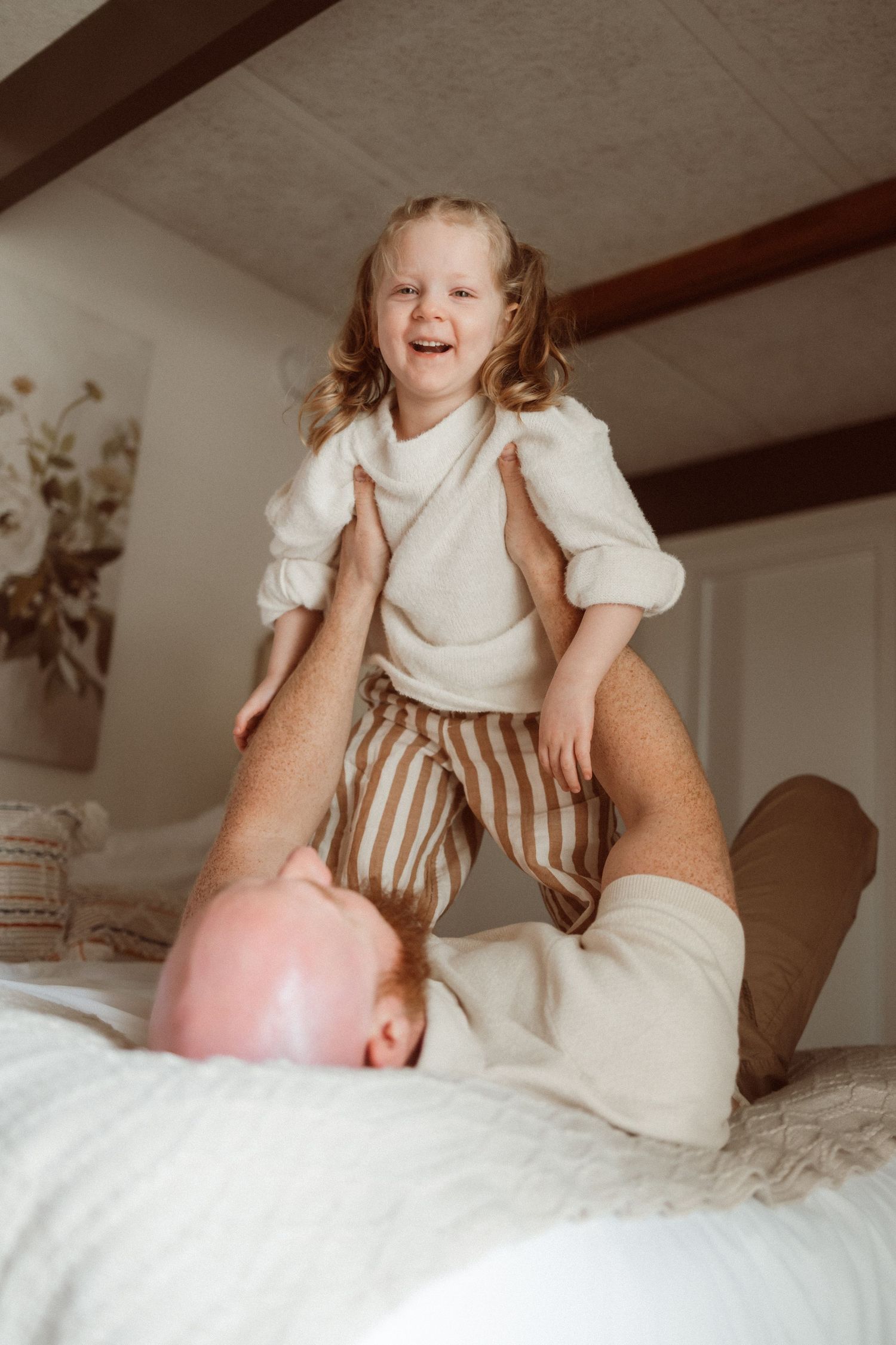 Playful moment between parent and child on bed with white decor.
