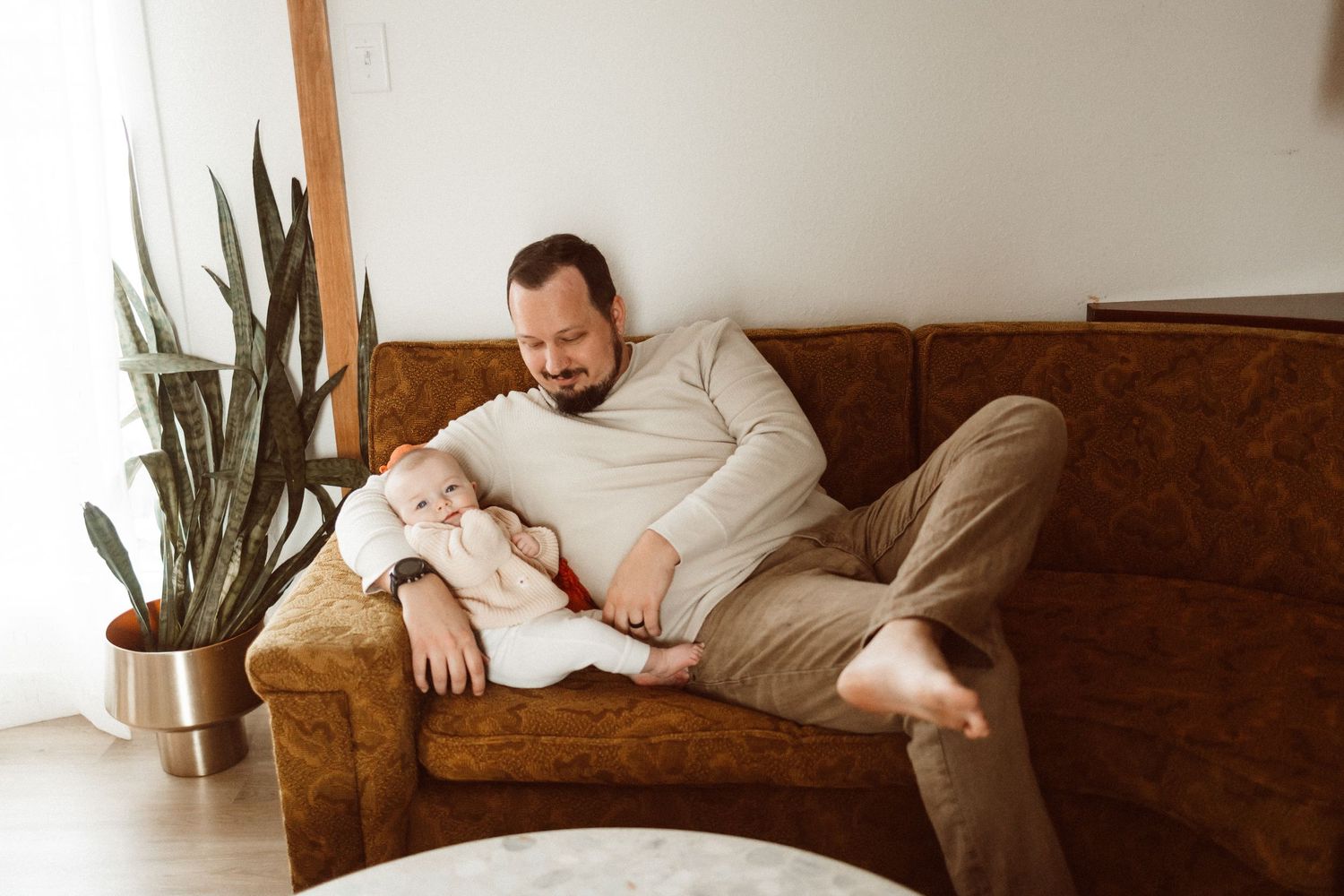Parent relaxing on brown leather couch with infant in casual home setting.