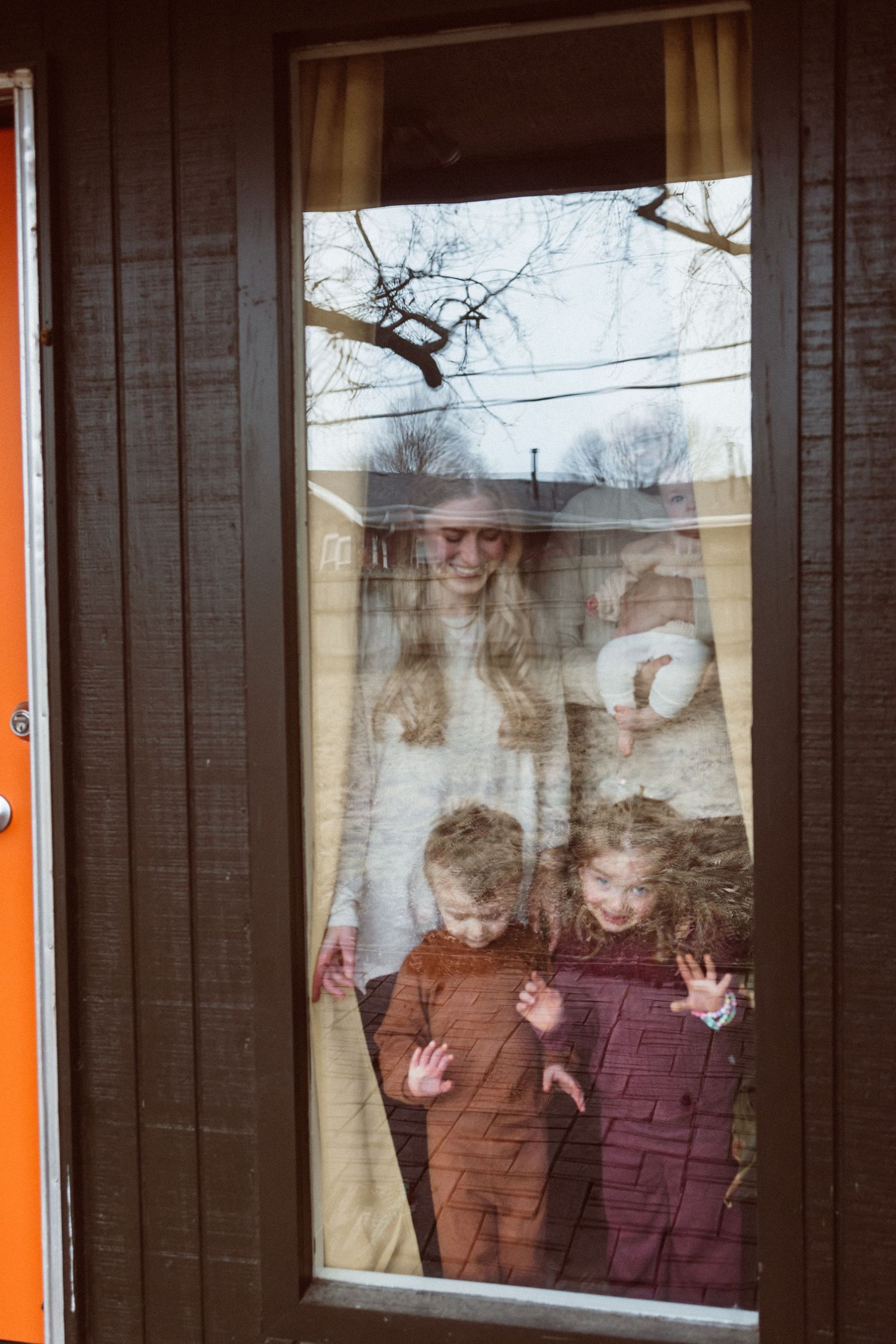 Children looking through window during winter with reflections creating dreamy atmosphere.