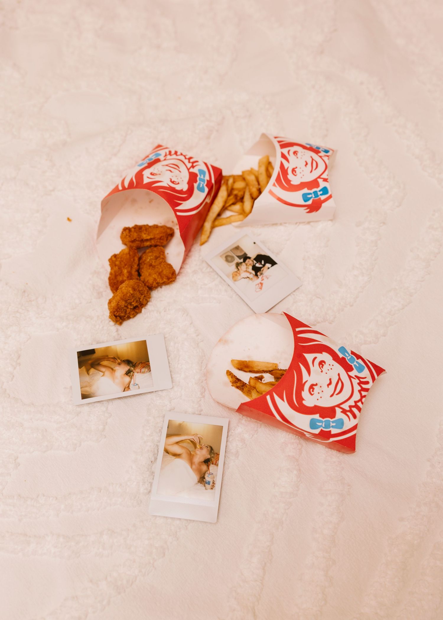 Wendy's fast food bags and wrappers scattered with vintage Polaroid photos and crispy chicken nuggets on a beige surface.