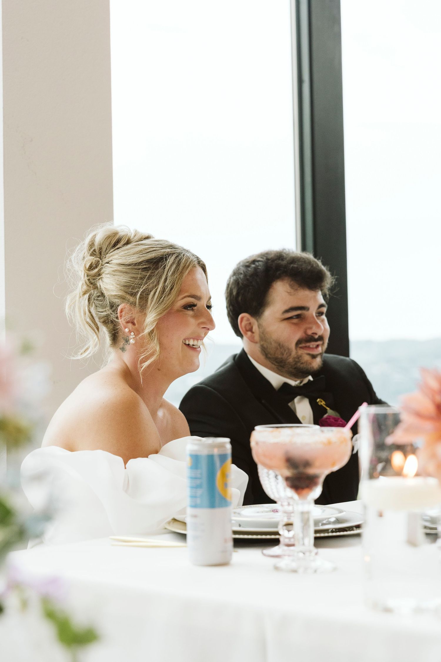 A happy couple at their wedding reception toasts with drinks at an elegant table setting.