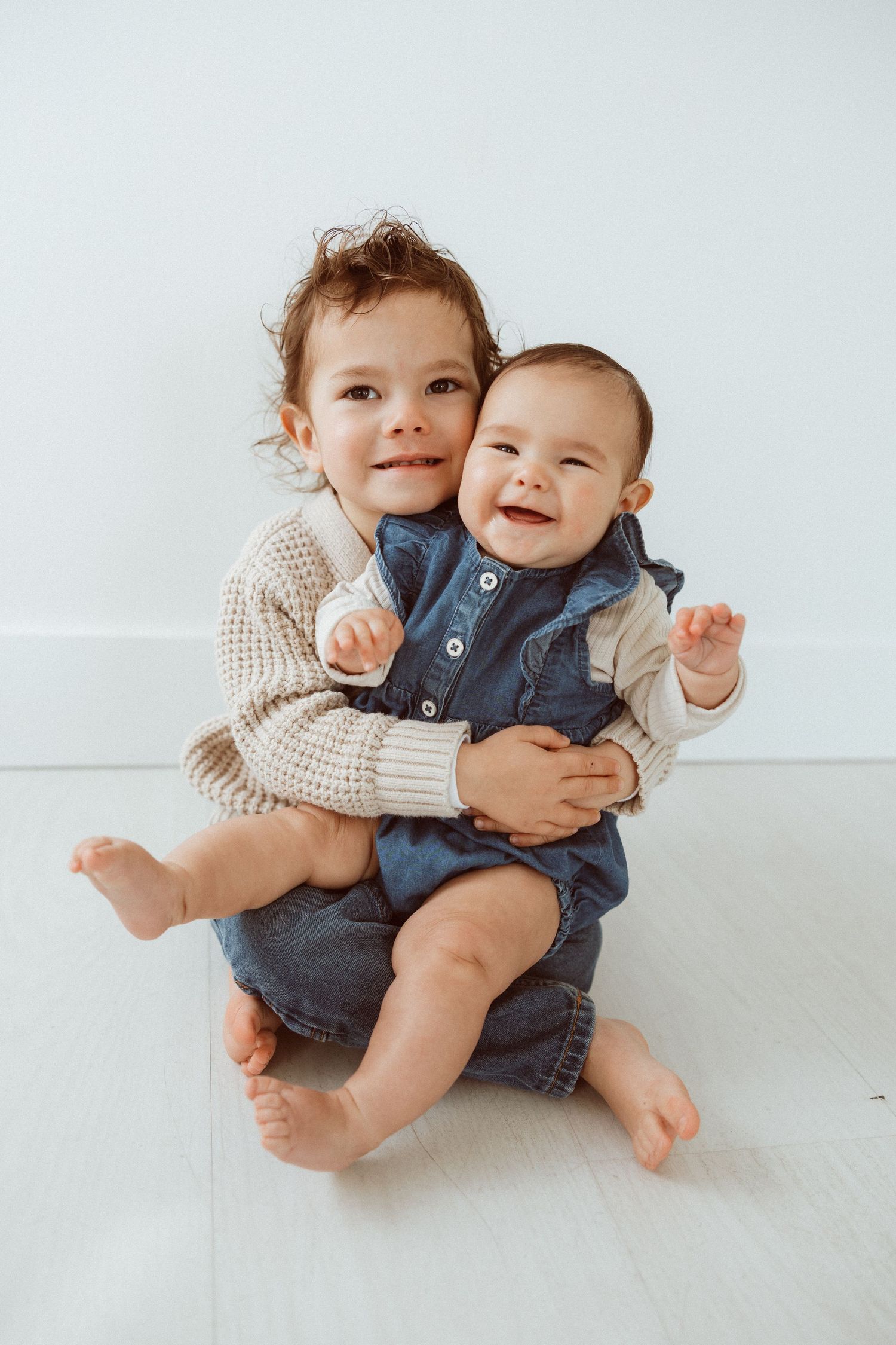 Two young siblings sharing sweet moment together against white background.