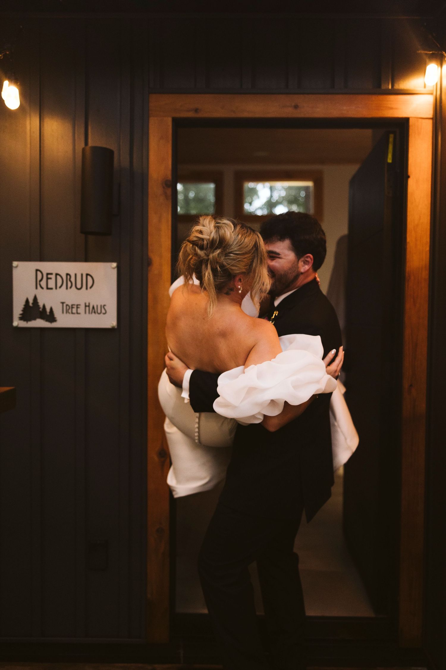 A couple shares an intimate moment in a dimly lit doorway at Redaud Tree House with warm lighting setting the mood.