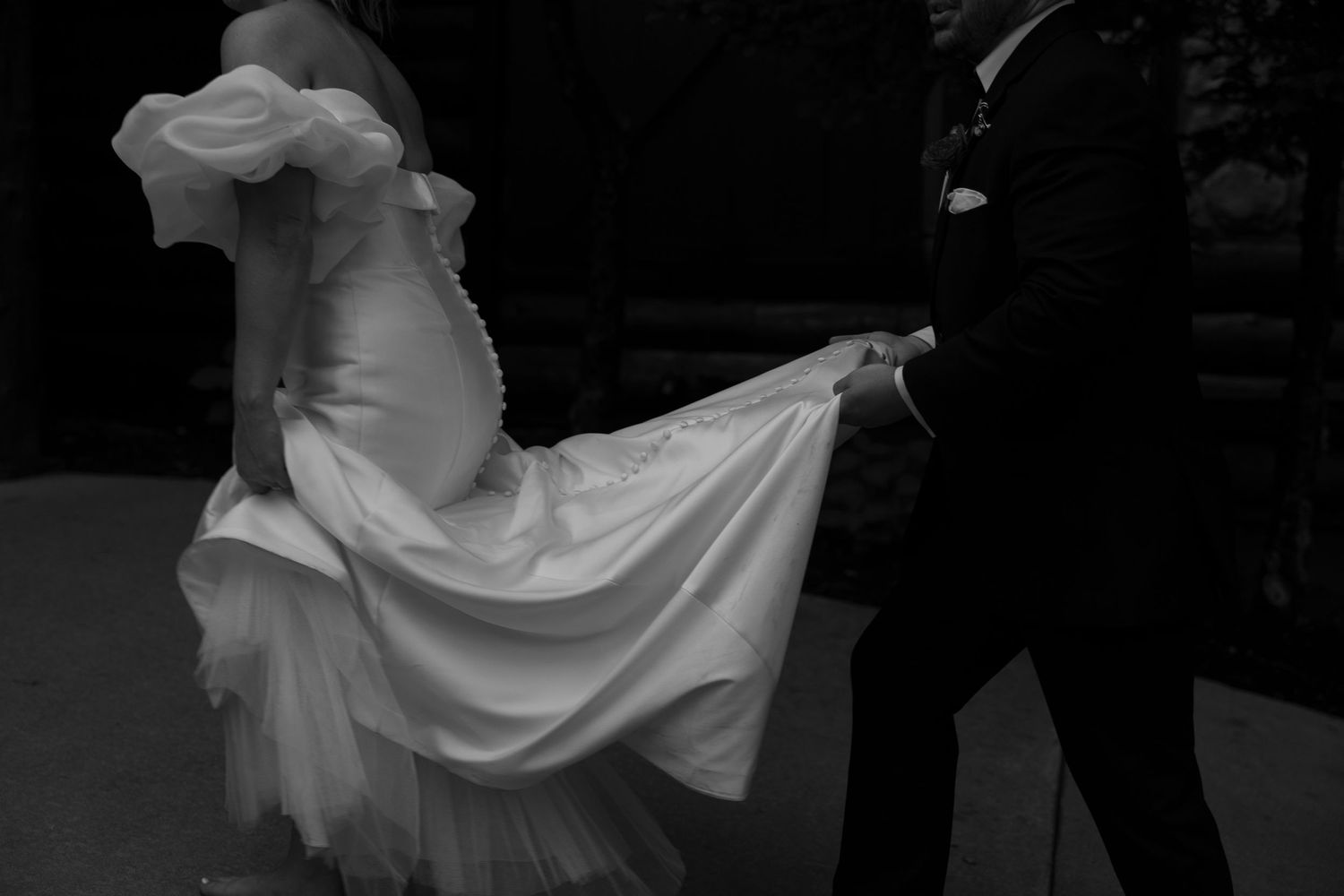Bride in white dress twirls playfully outdoors in black and white photo as her dress flows around her elegantly.