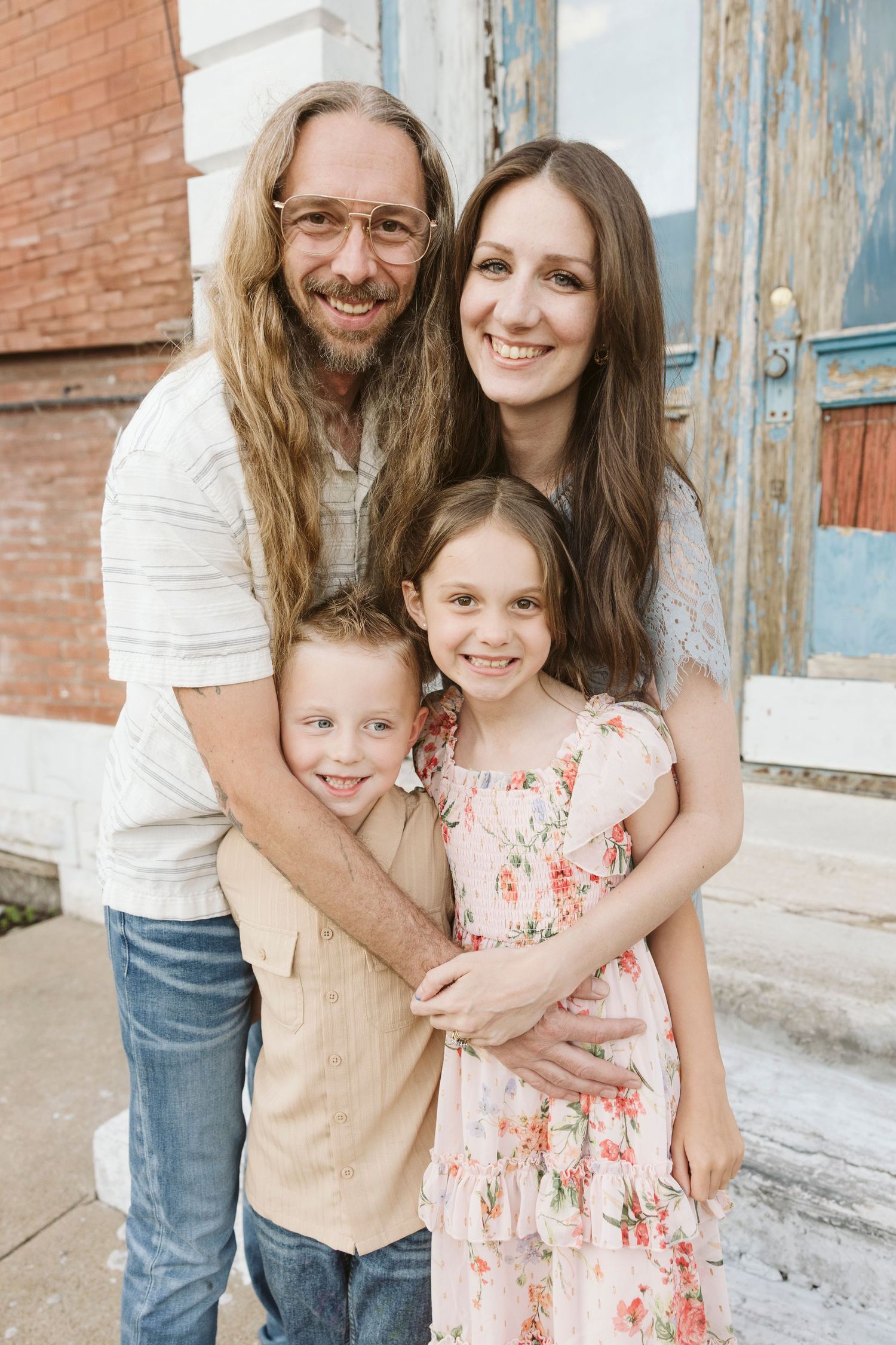 A family wearing white and floral outfits poses together against a rustic blue door background.
