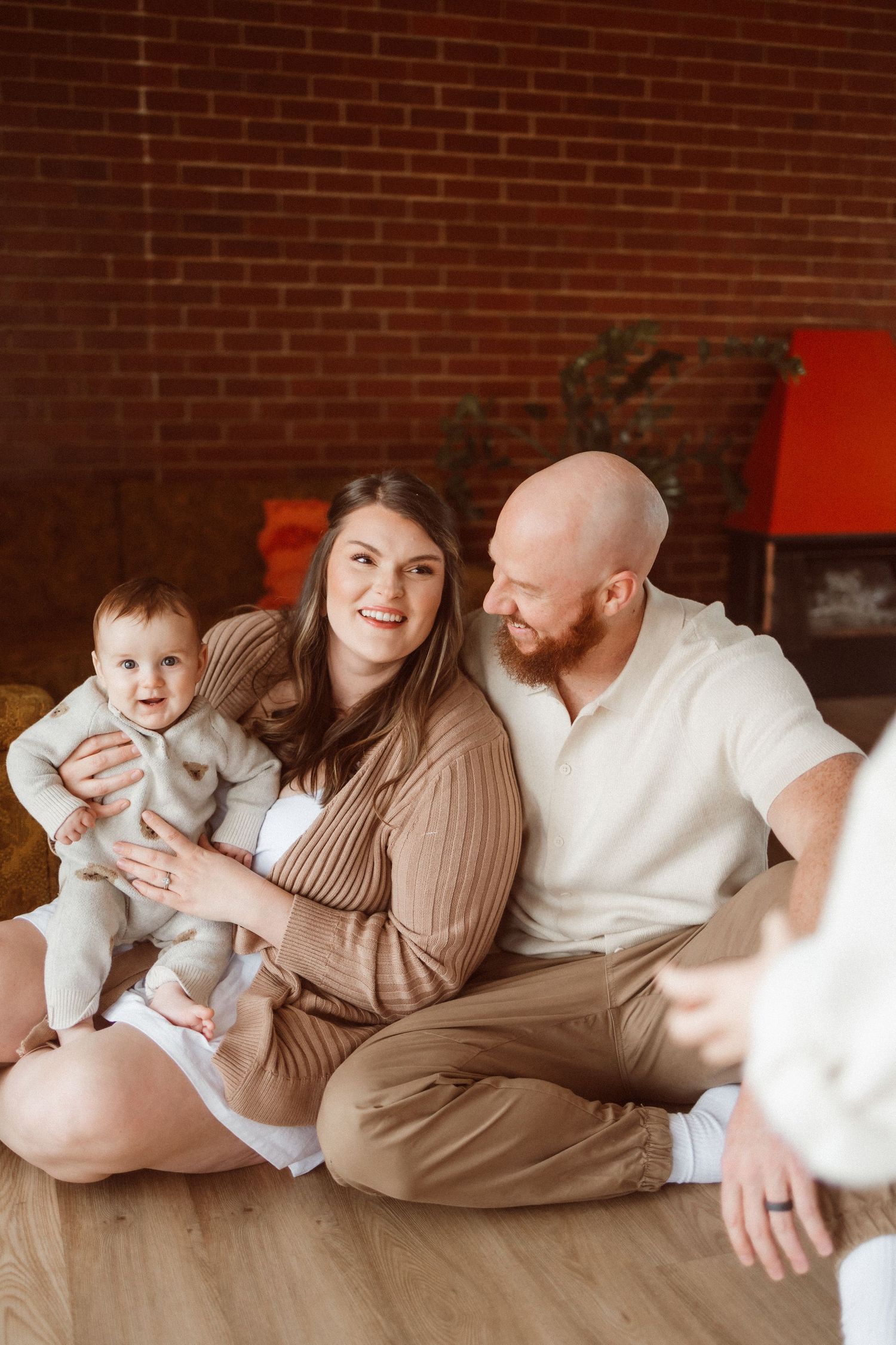 Candid lifestyle family photos showing relaxed moments against rustic brick backdrop.