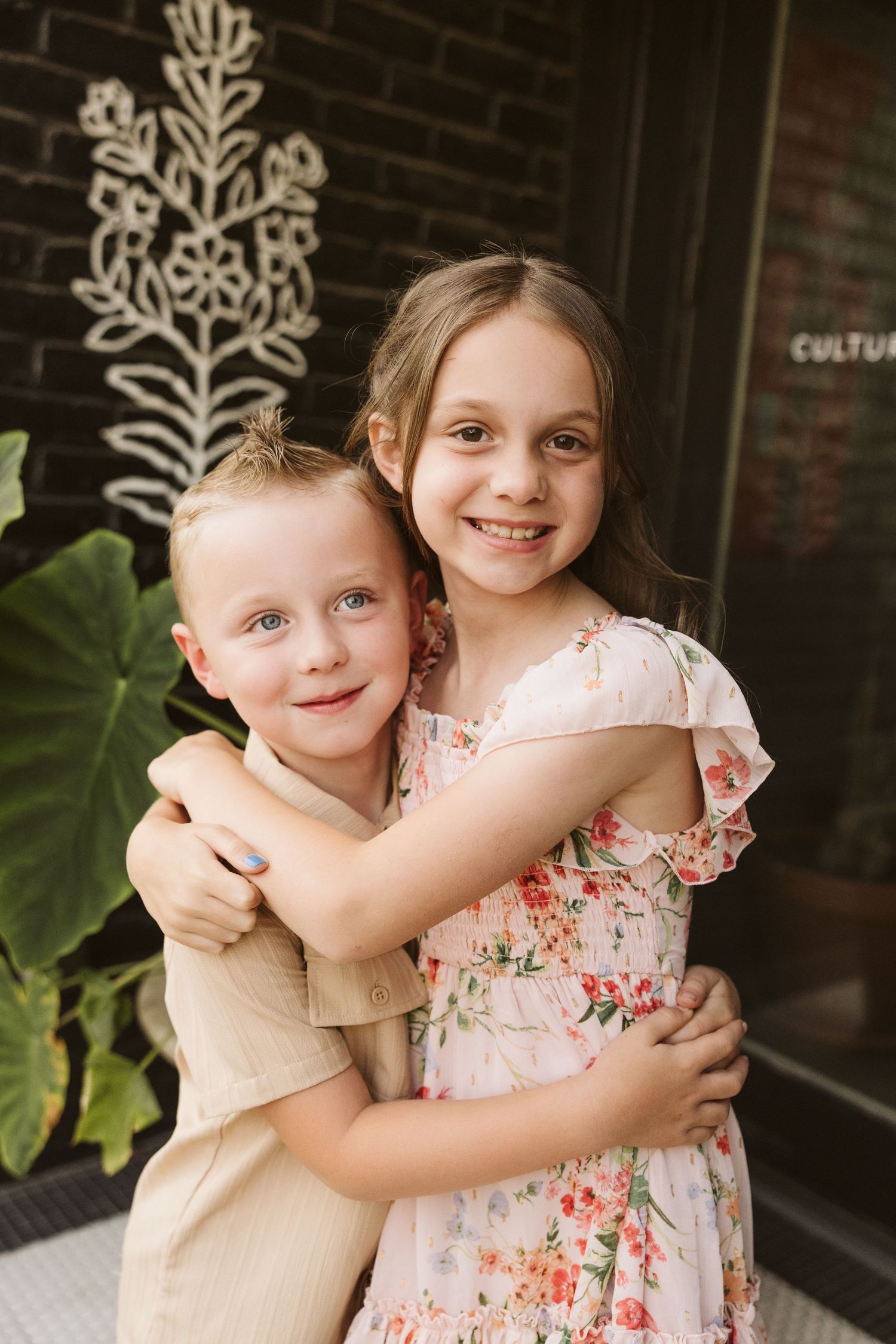 Children hugging and smiling on a porch with decorative wall designs.