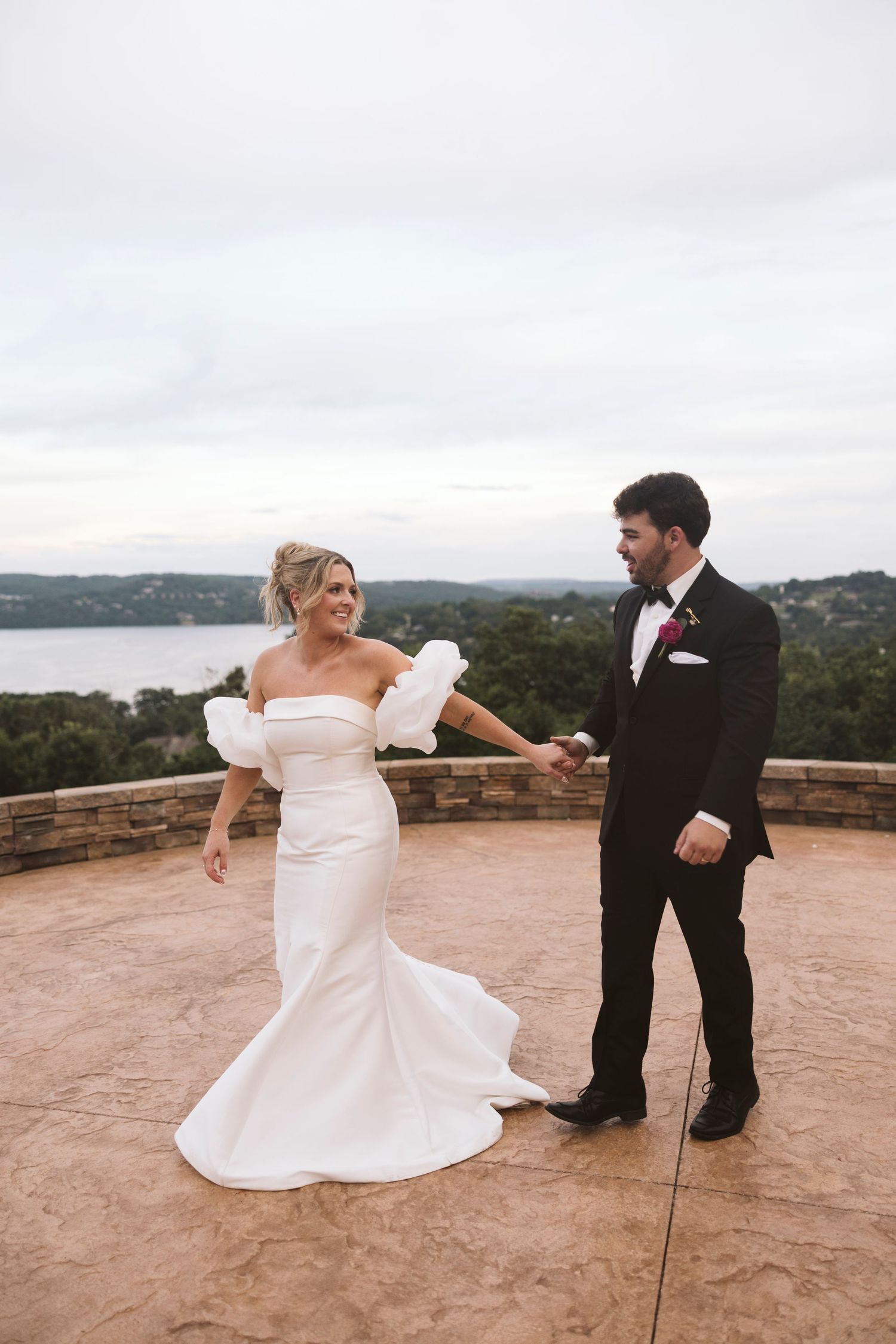 A couple shares a joyful moment on a stone terrace overlooking a scenic lake view.