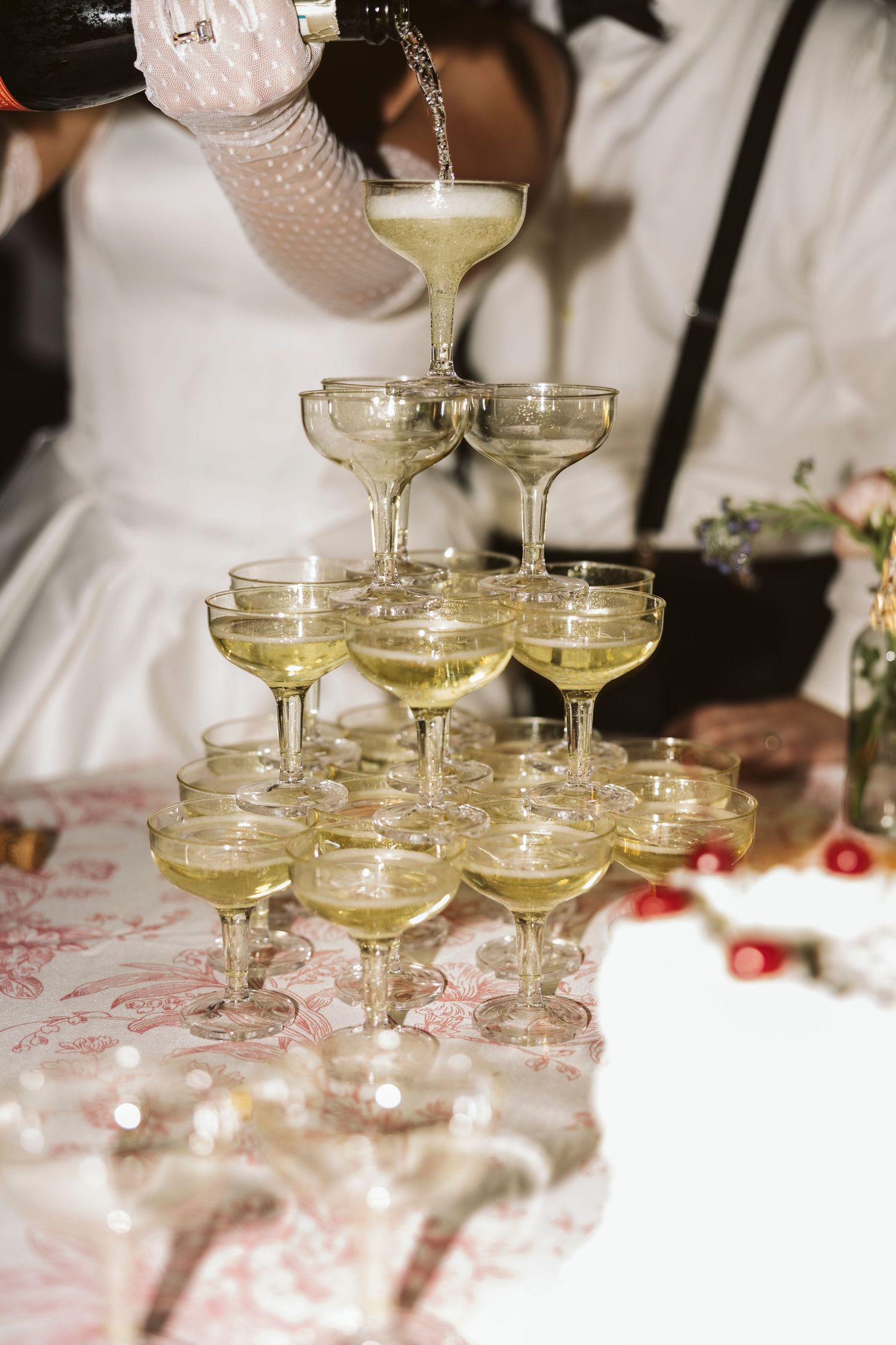 A champagne tower being filled with sparkling wine at an elegant wedding reception.