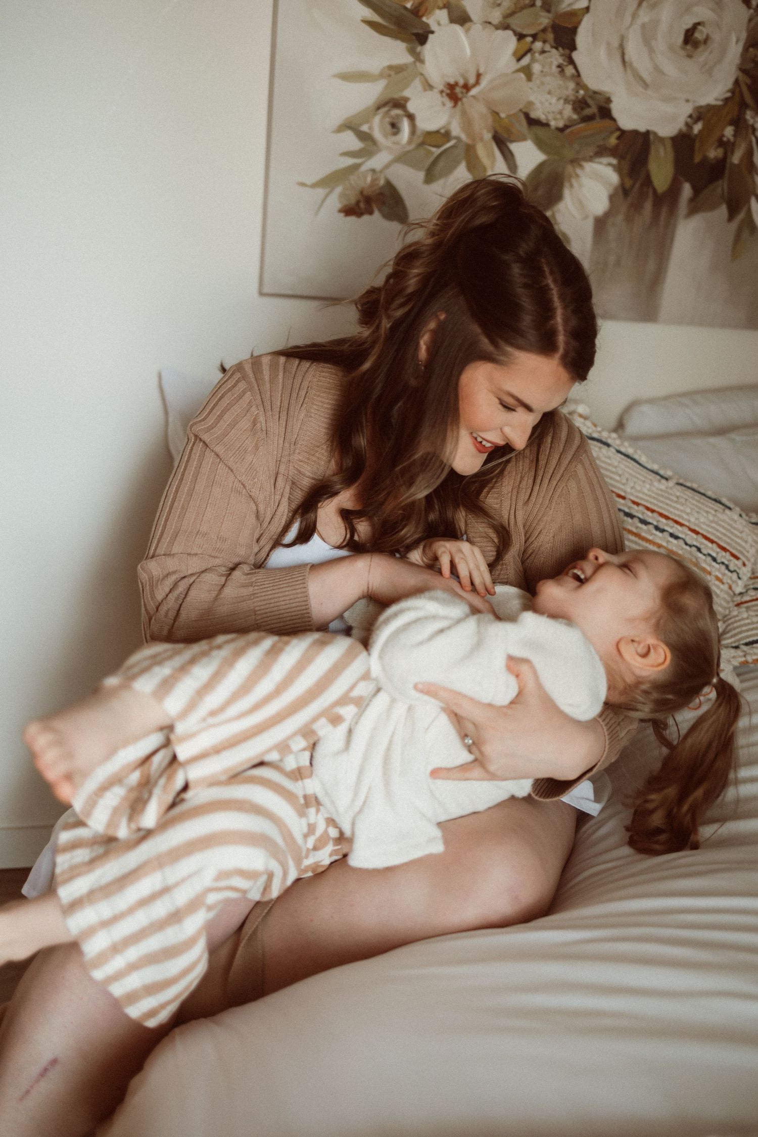 Intimate moment between parent and child relaxing on bed with floral artwork in background.