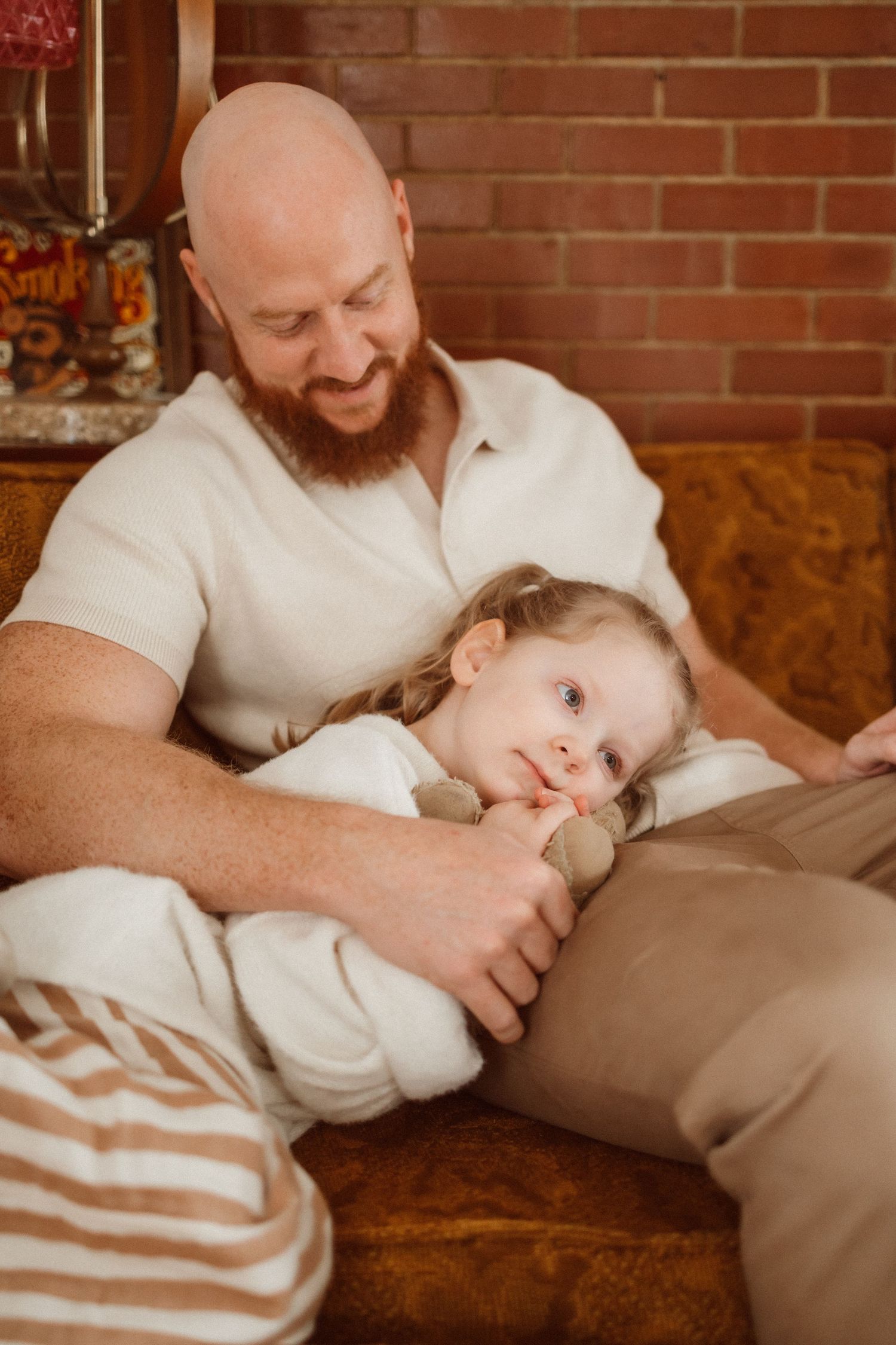 Intimate family moments captured on couch with brick wall backdrop.