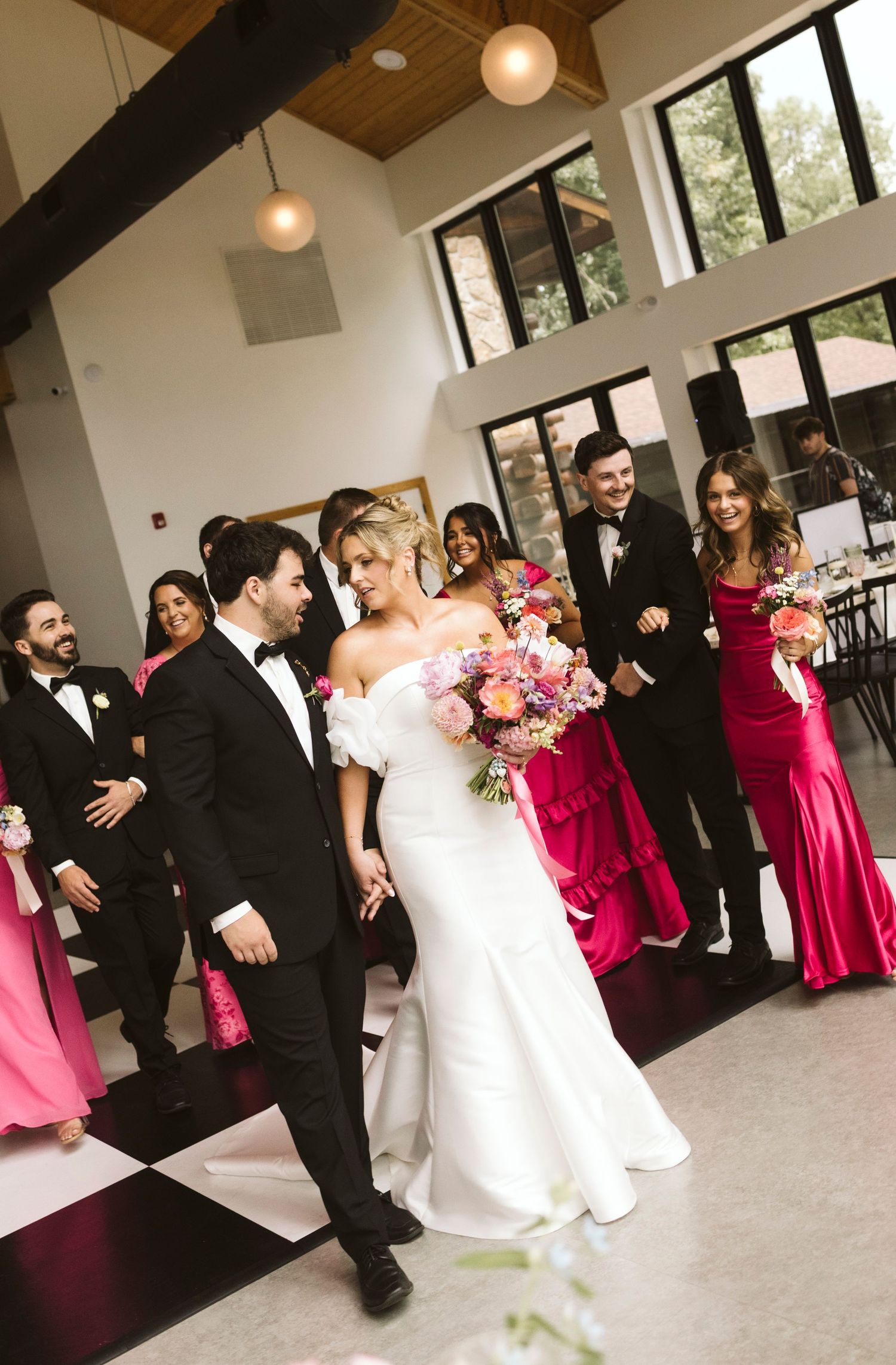 Wedding party dancing and celebrating in a modern venue with high ceilings.