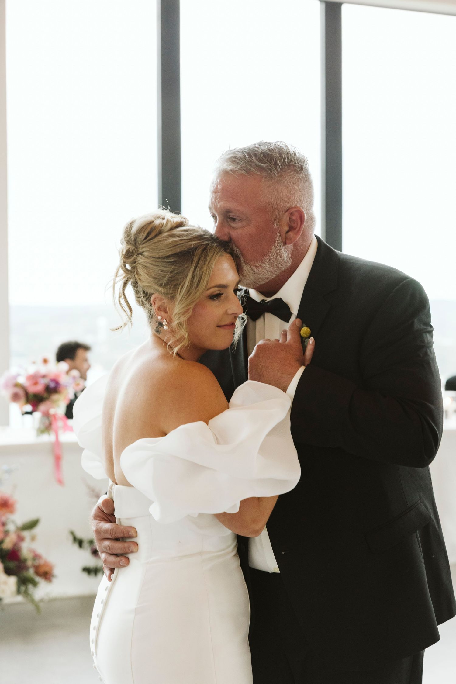 A tender dance moment during a wedding celebration with white decor and floral arrangements visible.