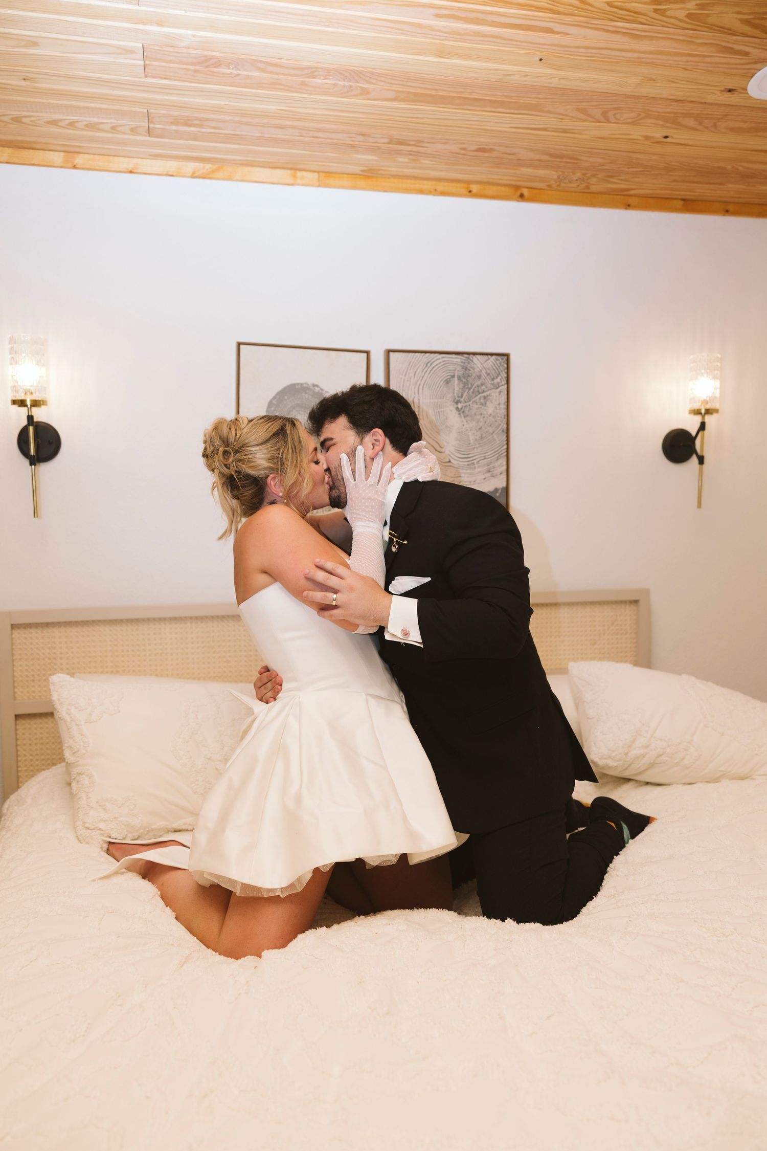 The bride and groom share a romantic moment lying on a plush white bed in these wedding photos.
