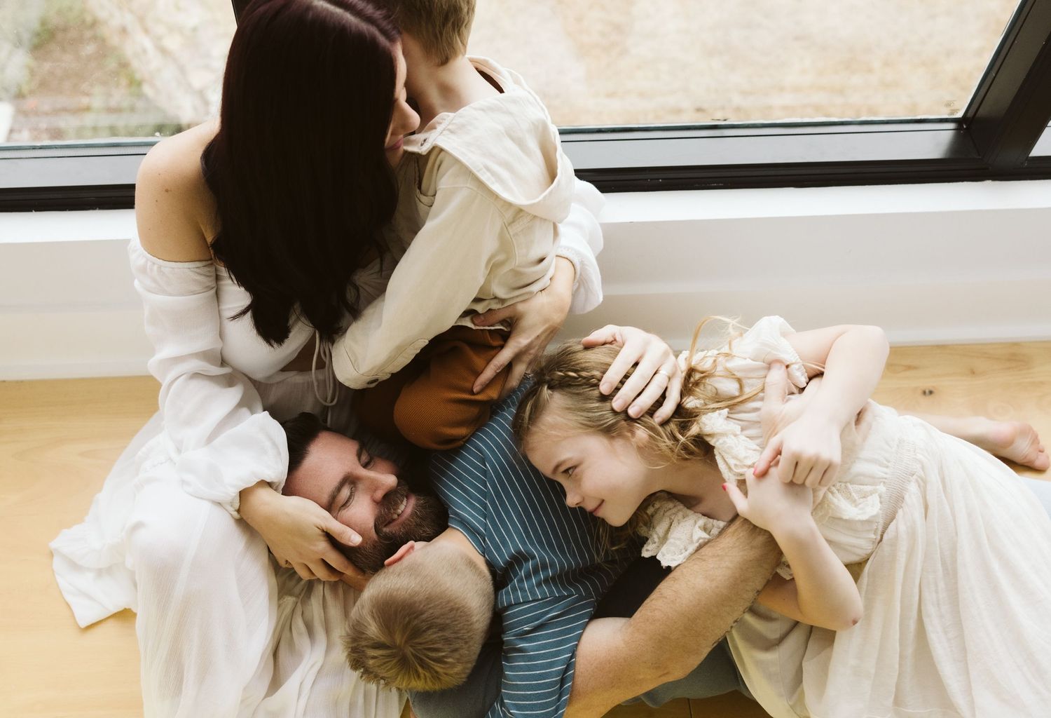 Candid family moment captured while cuddling together on the floor near a window.