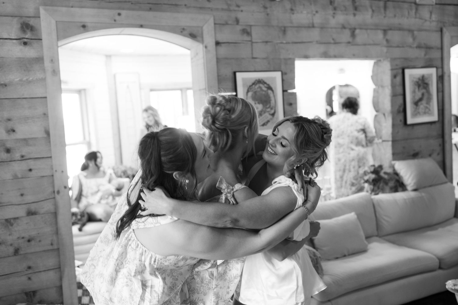 A group of people in formal attire embracing and laughing together on a couch in a rustic room with wooden walls.