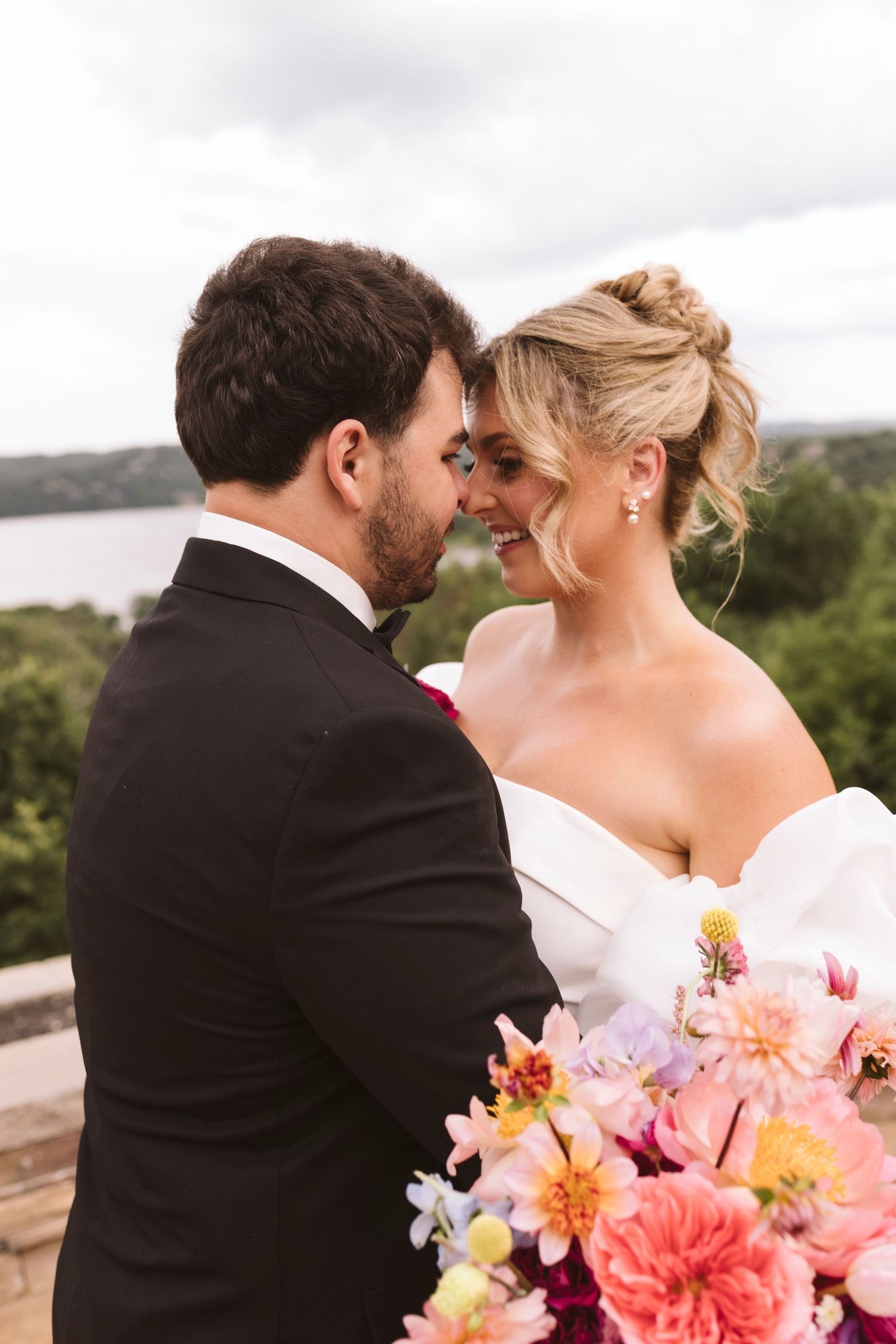 Romantic wedding moment captured outdoors with vibrant coral and pink floral bouquet.
