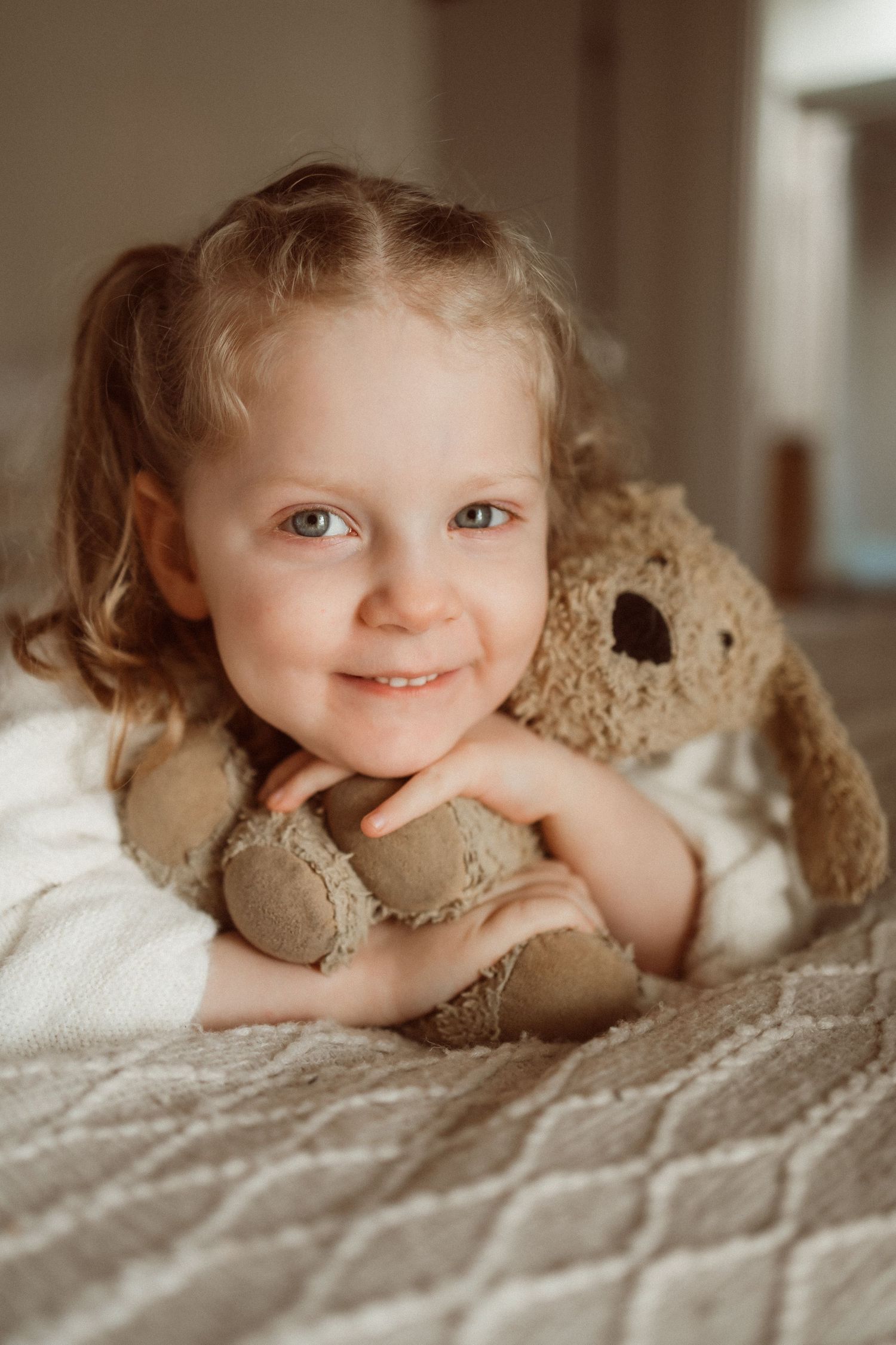 Child cuddling with stuffed bunny toy on textured bedding.