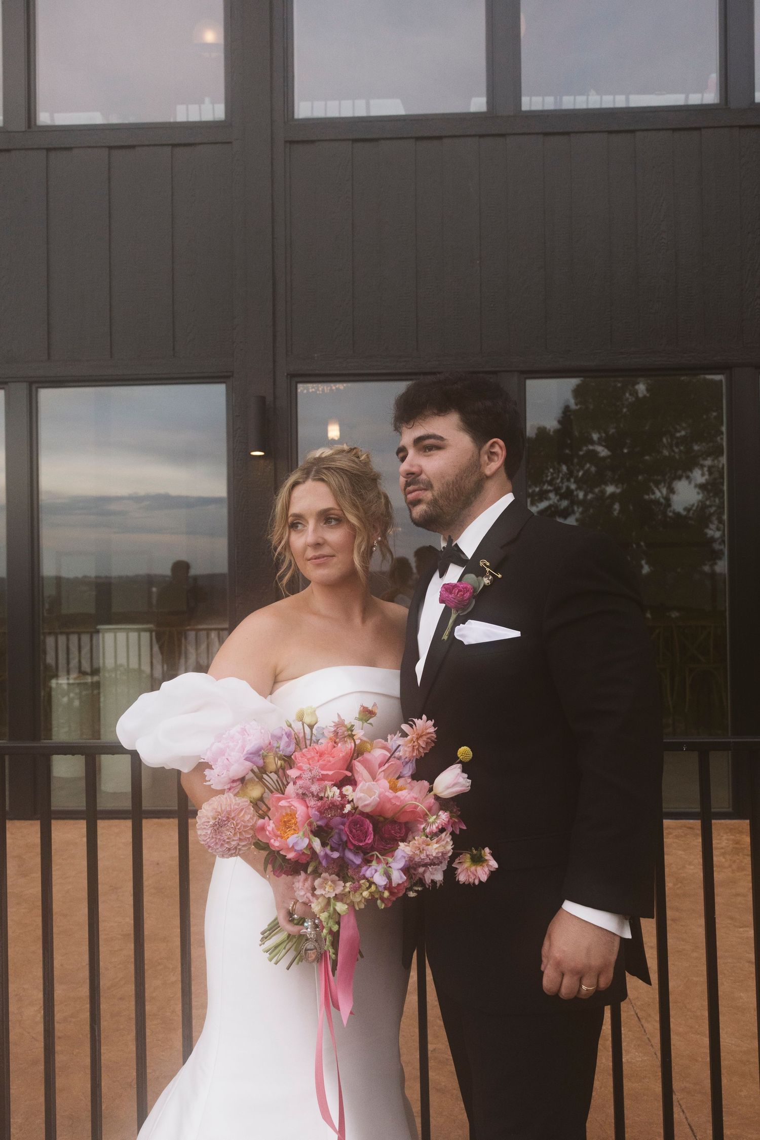 A couple poses for formal wedding portraits against modern architecture with a vibrant bouquet.