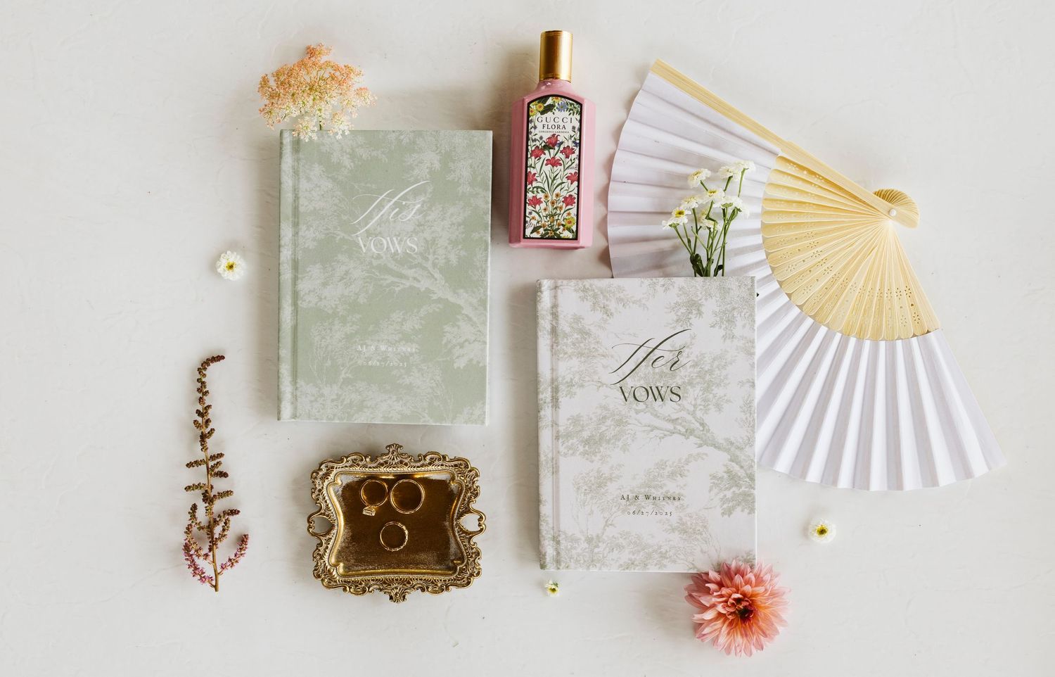 Flat lay of elegant wedding stationery with fan, dried flowers, and decorative bottle on white background.