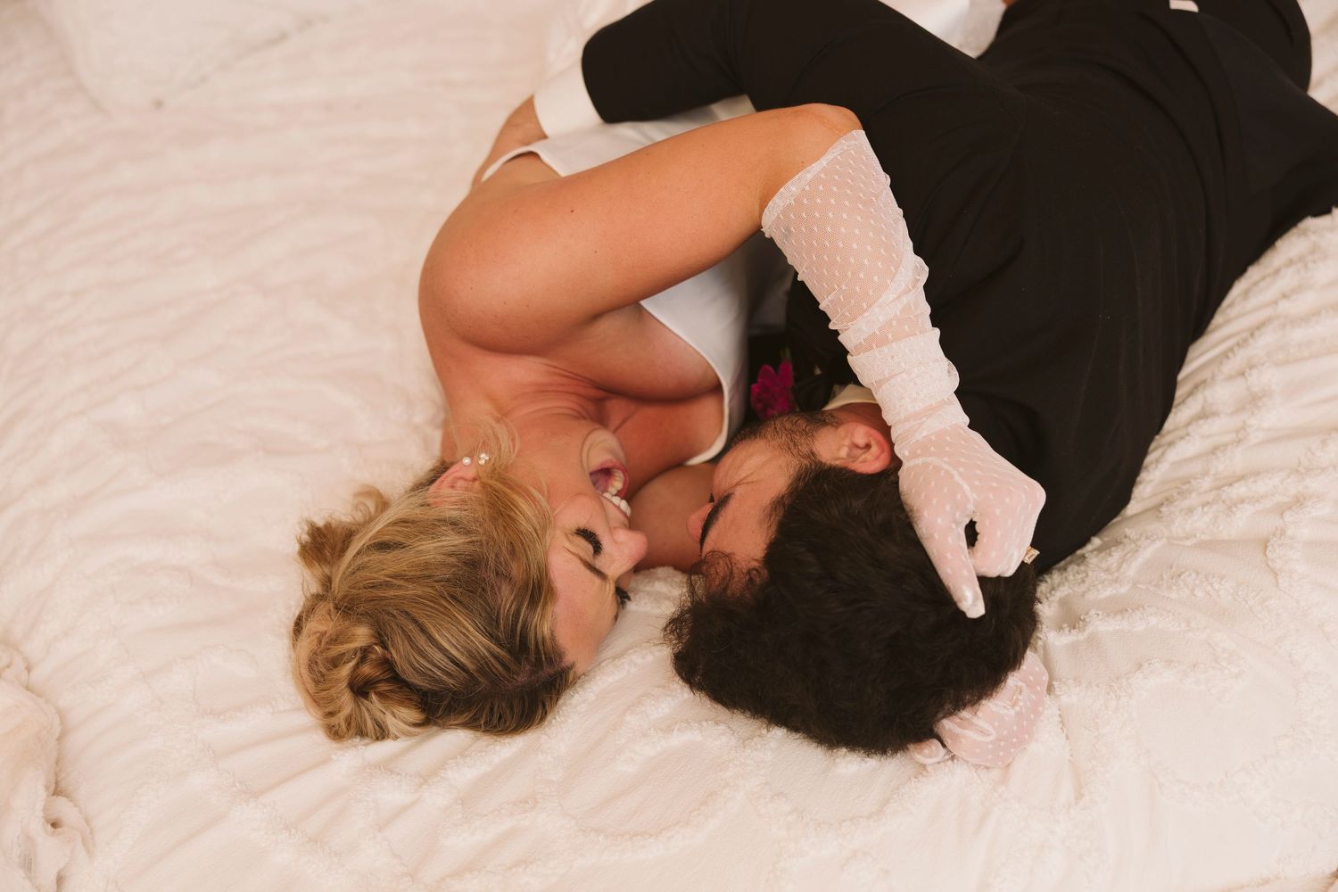 Two people lying close together on white bedding while sharing an intimate moment.