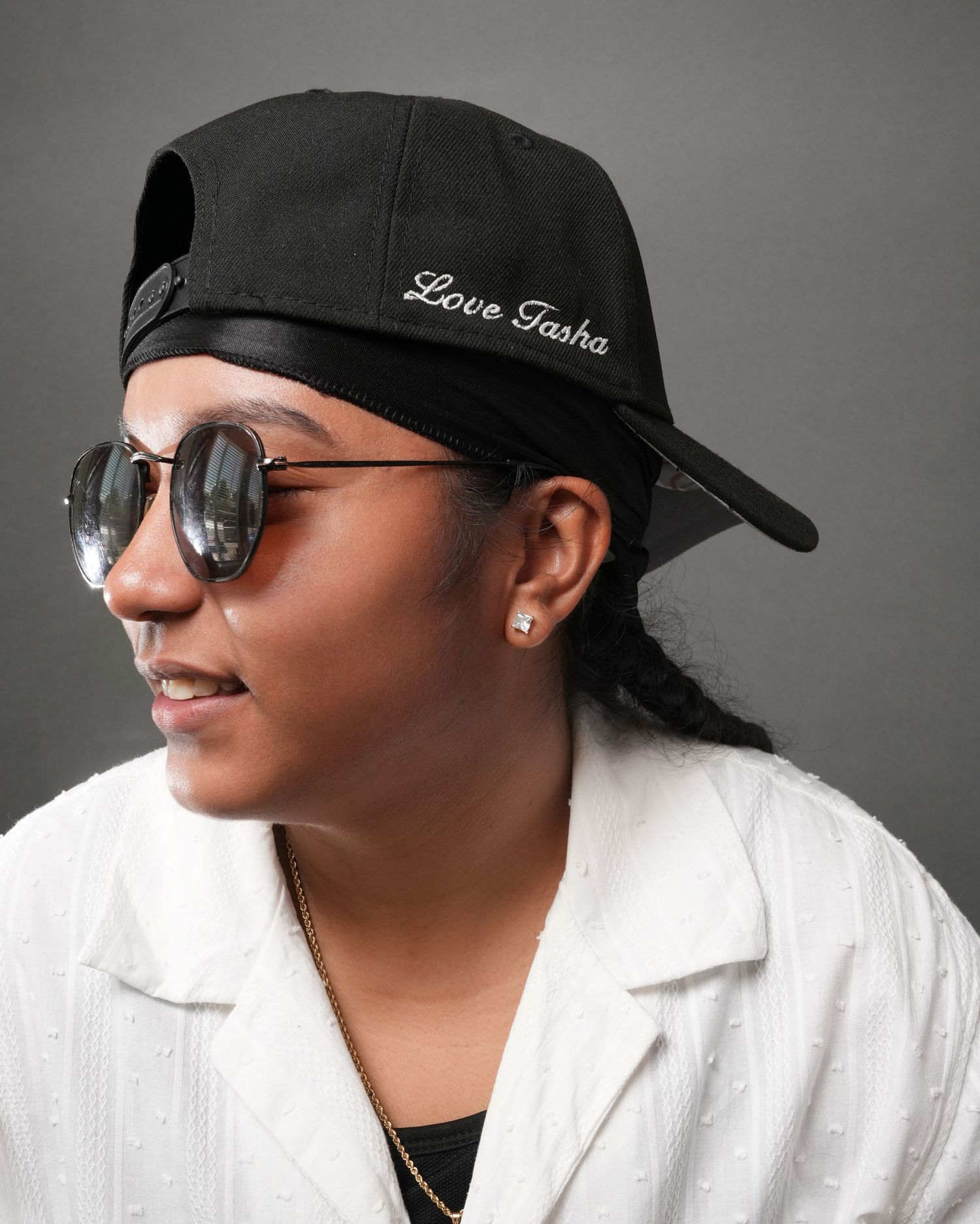Close-up portrait of a person wearing Love Tastes baseball cap and sunglasses against gray background.