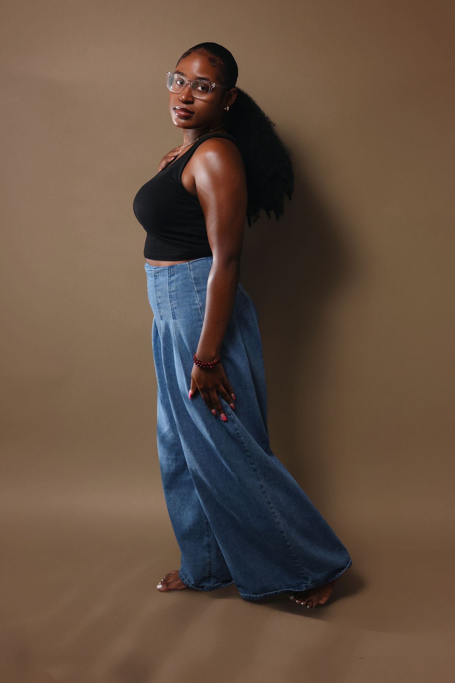 Side view portrait of a person in casual outfit posing against brown studio background.
