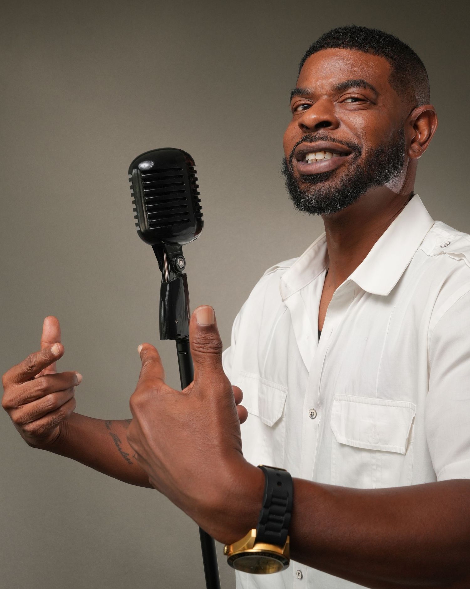 Performer in white shirt holds vintage microphone while gesturing expressively against neutral background.